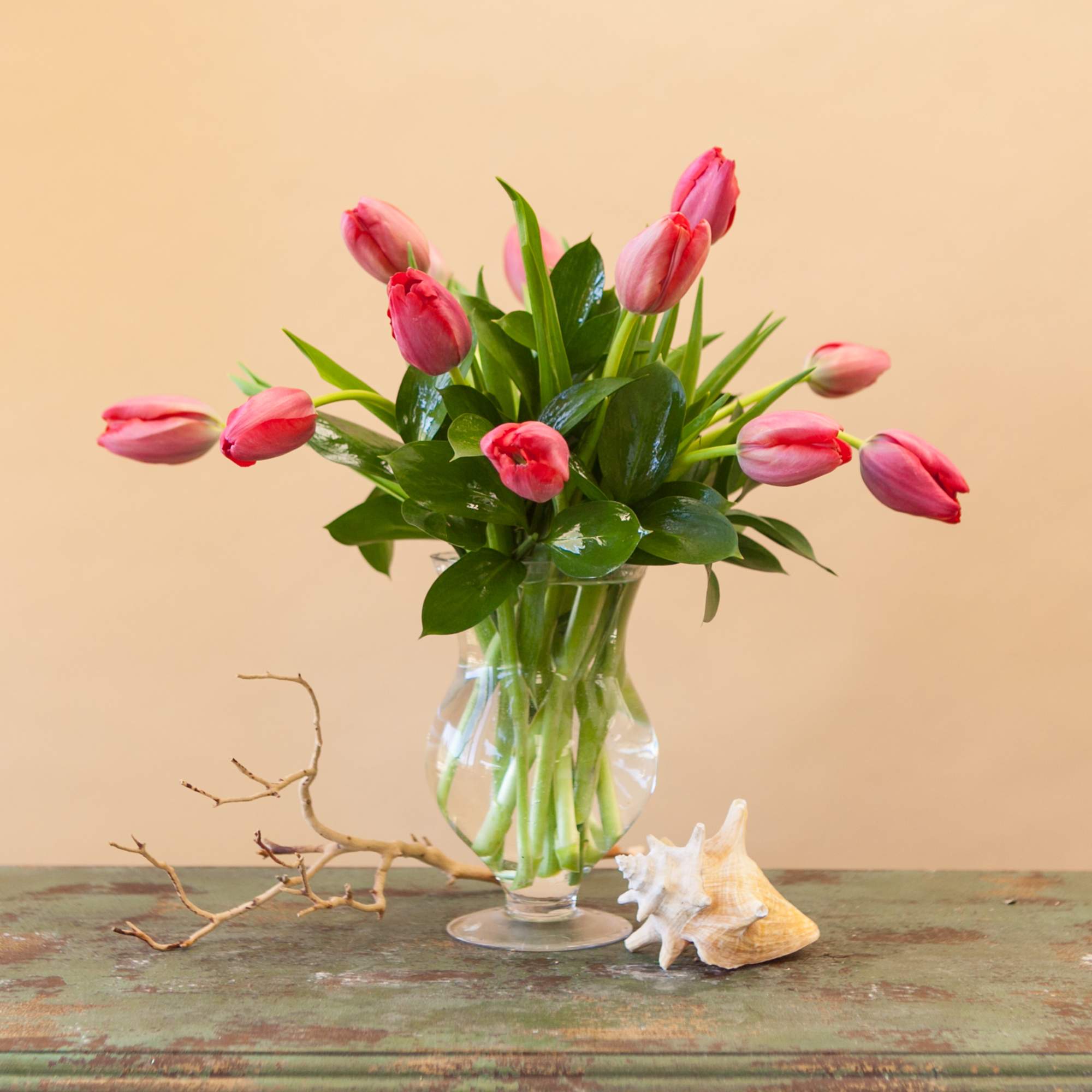 Pink tulips in a clear glass vase on a rustic table
