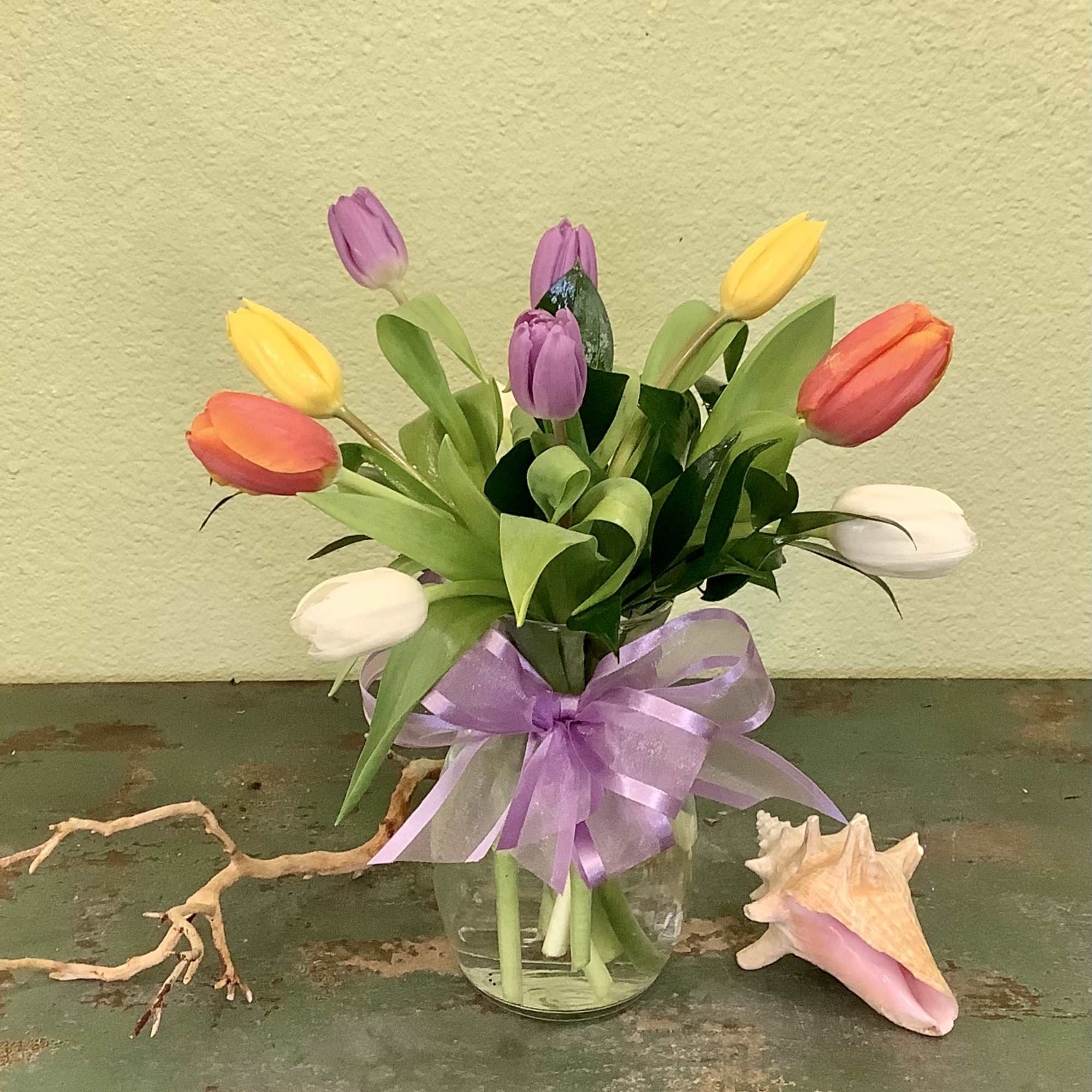 Bouquet of multicolored tulips in a glass vase with a purple ribbon