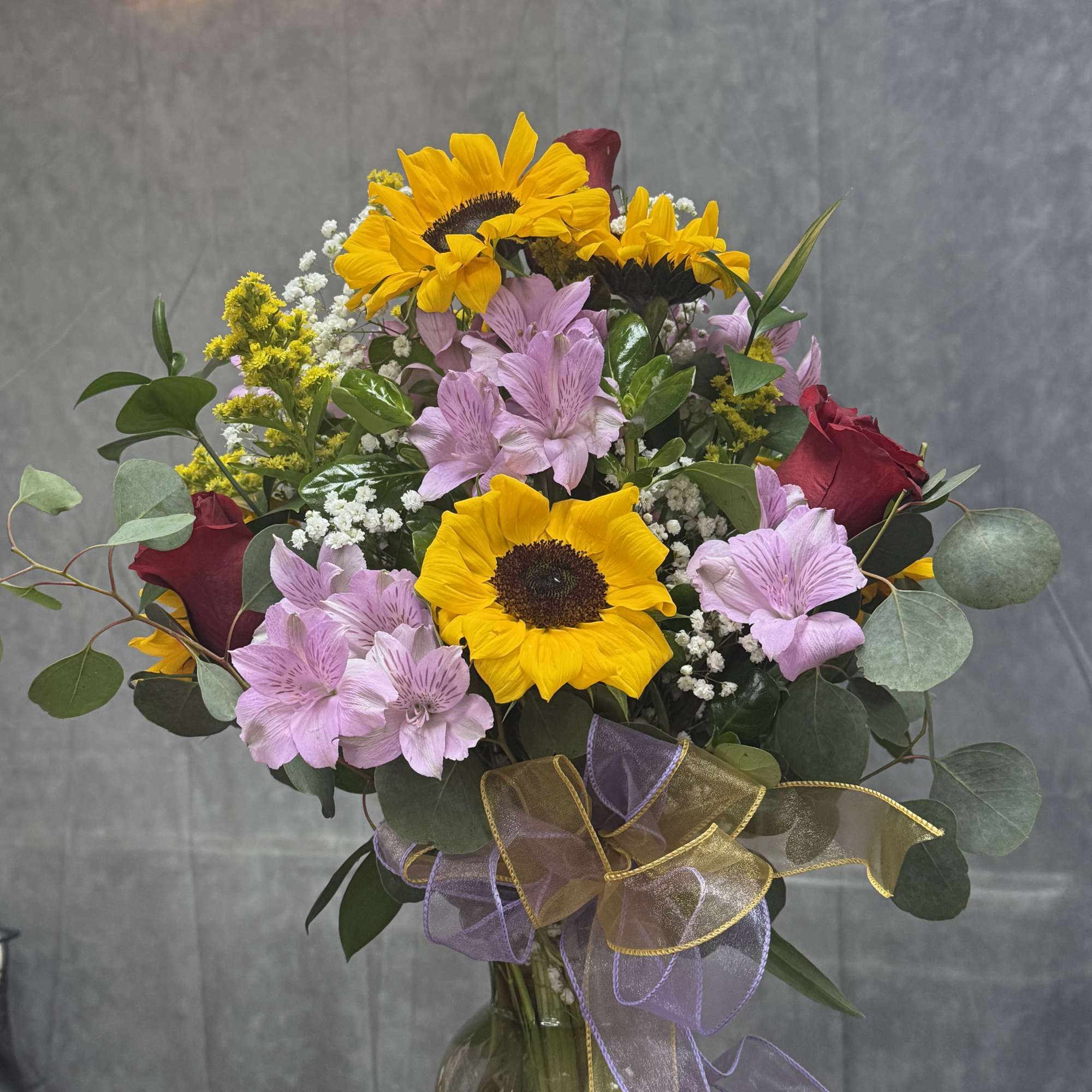 Bouquet of sunflowers, pink alstroemeria, and red roses in a glass vase