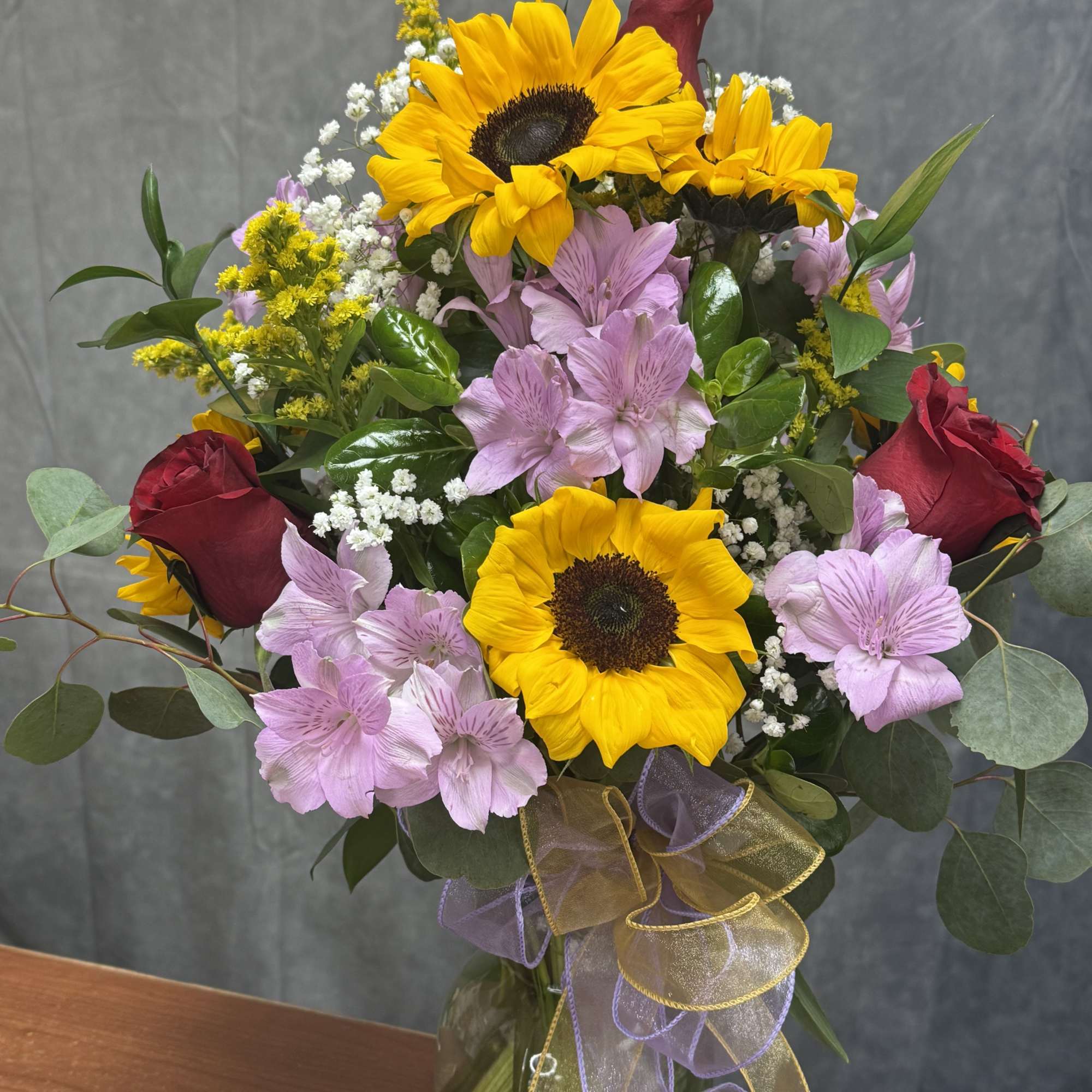 Bouquet of sunflowers, pink alstroemeria, and red roses in a glass vase
