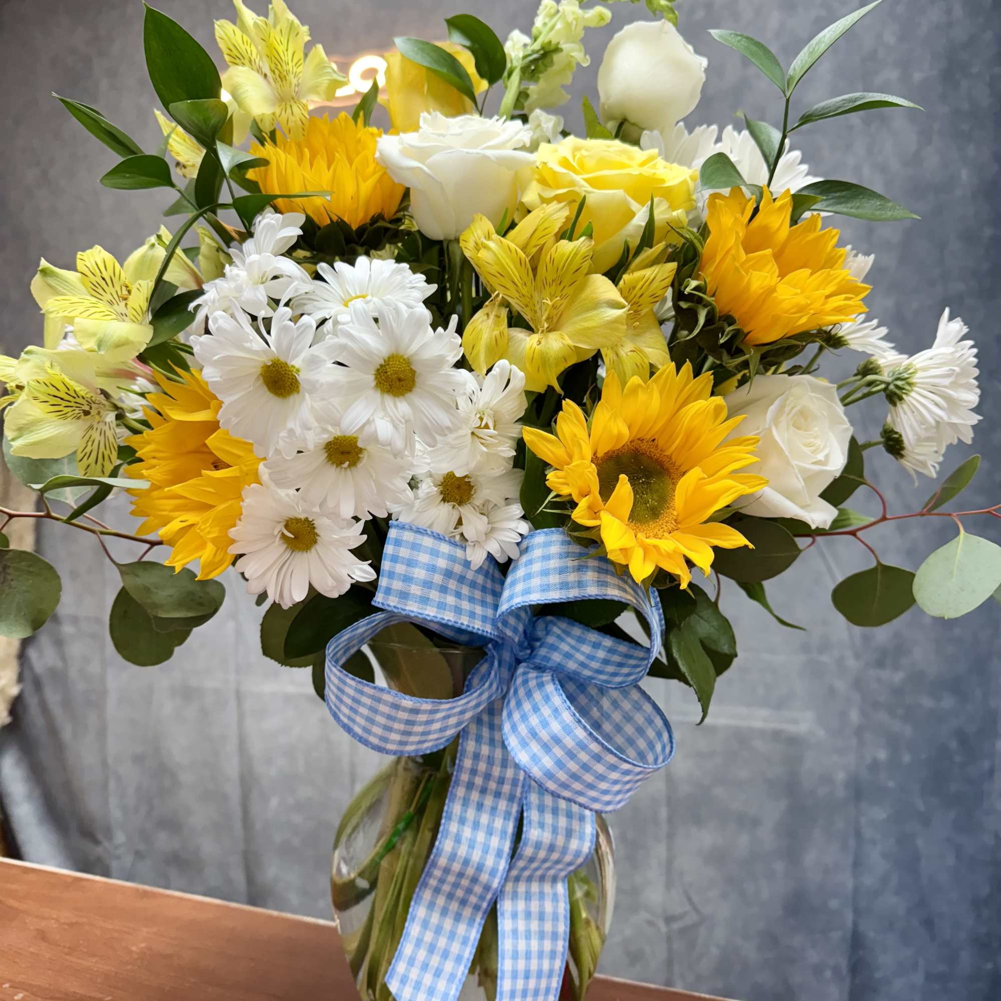 Yellow and white mixed bouquet in a glass vase with a blue gingham ribbon