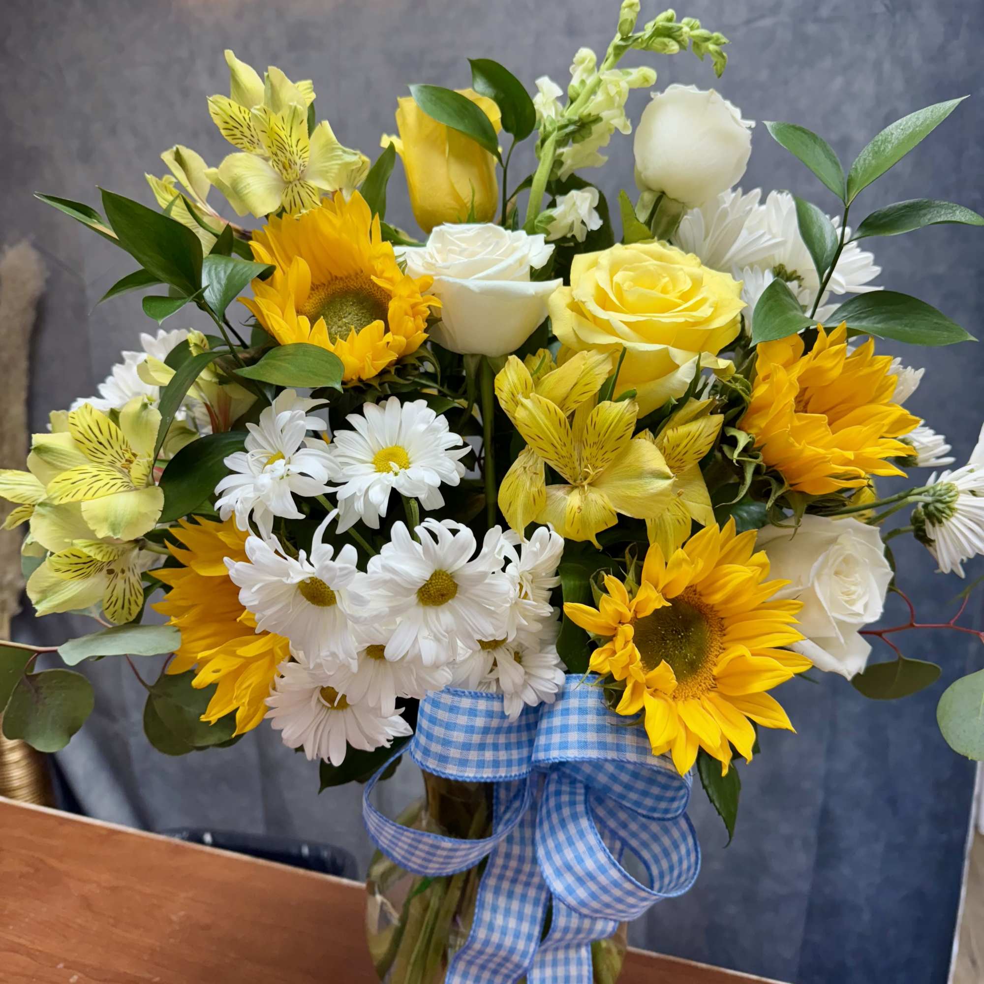Yellow and white mixed bouquet in a glass vase with a blue ribbon