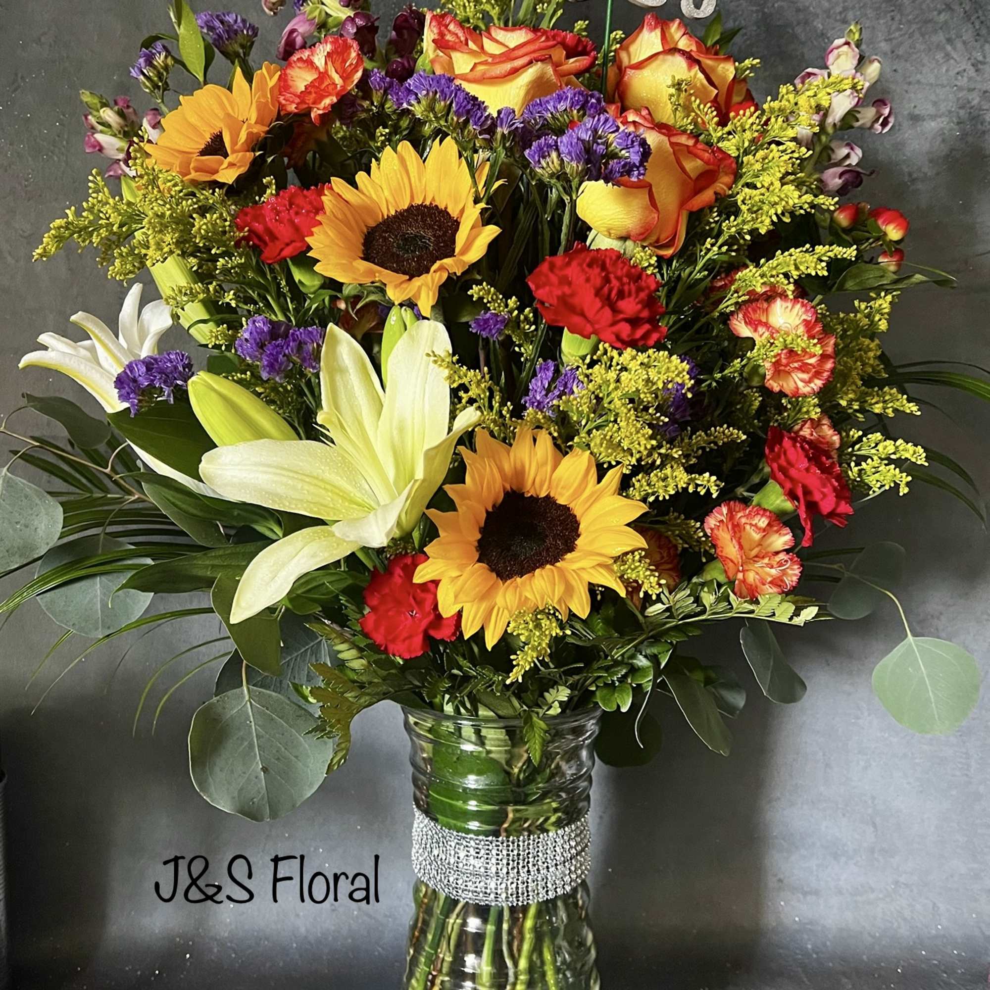 Mixed bouquet with sunflowers, roses, lilies, and carnations in a glass vase