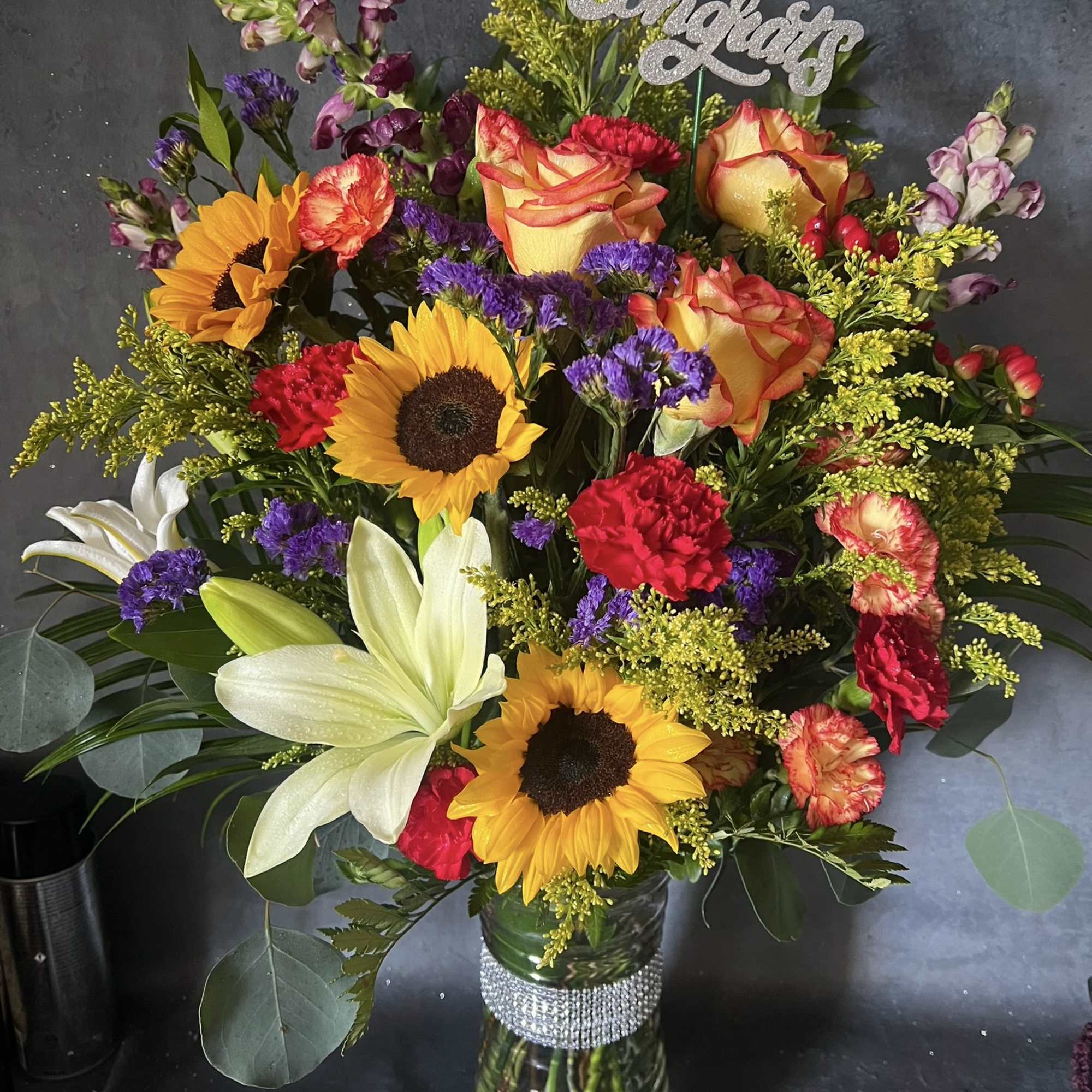 Colorful mixed bouquet in a glass vase with a glittery "Congrats" sign