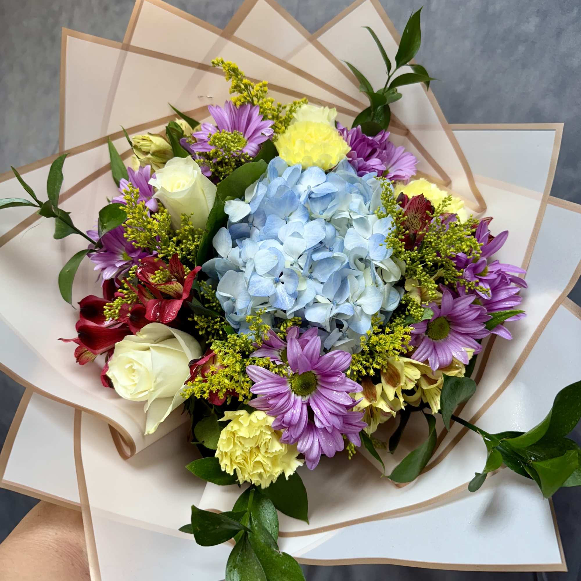 Bouquet with blue hydrangea, purple daisies, and white roses in paper wrap