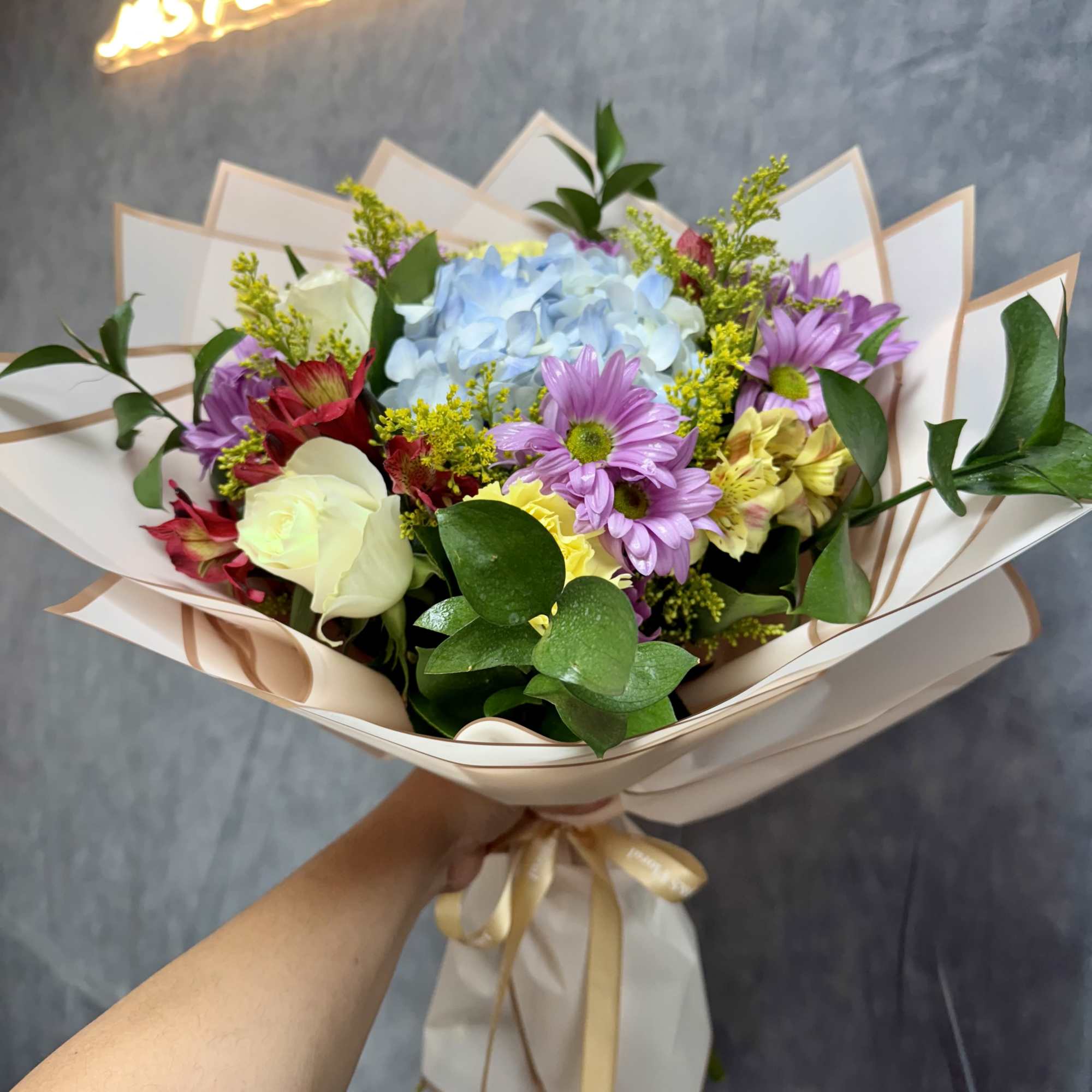 Handheld bouquet of pastel flowers wrapped in cream paper