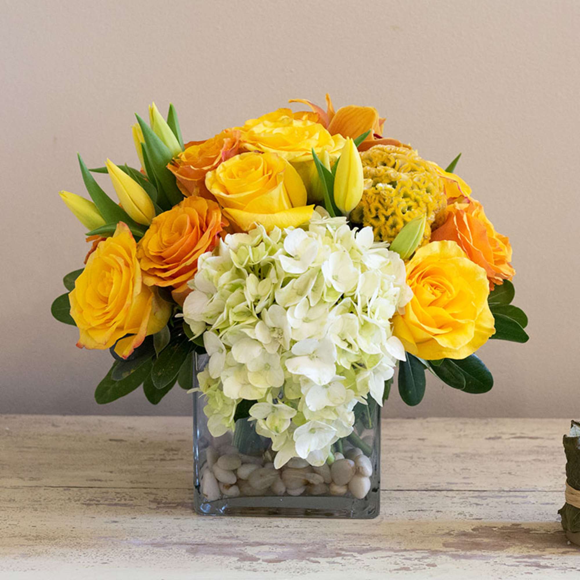 Yellow and orange roses with white hydrangea in a square glass vase