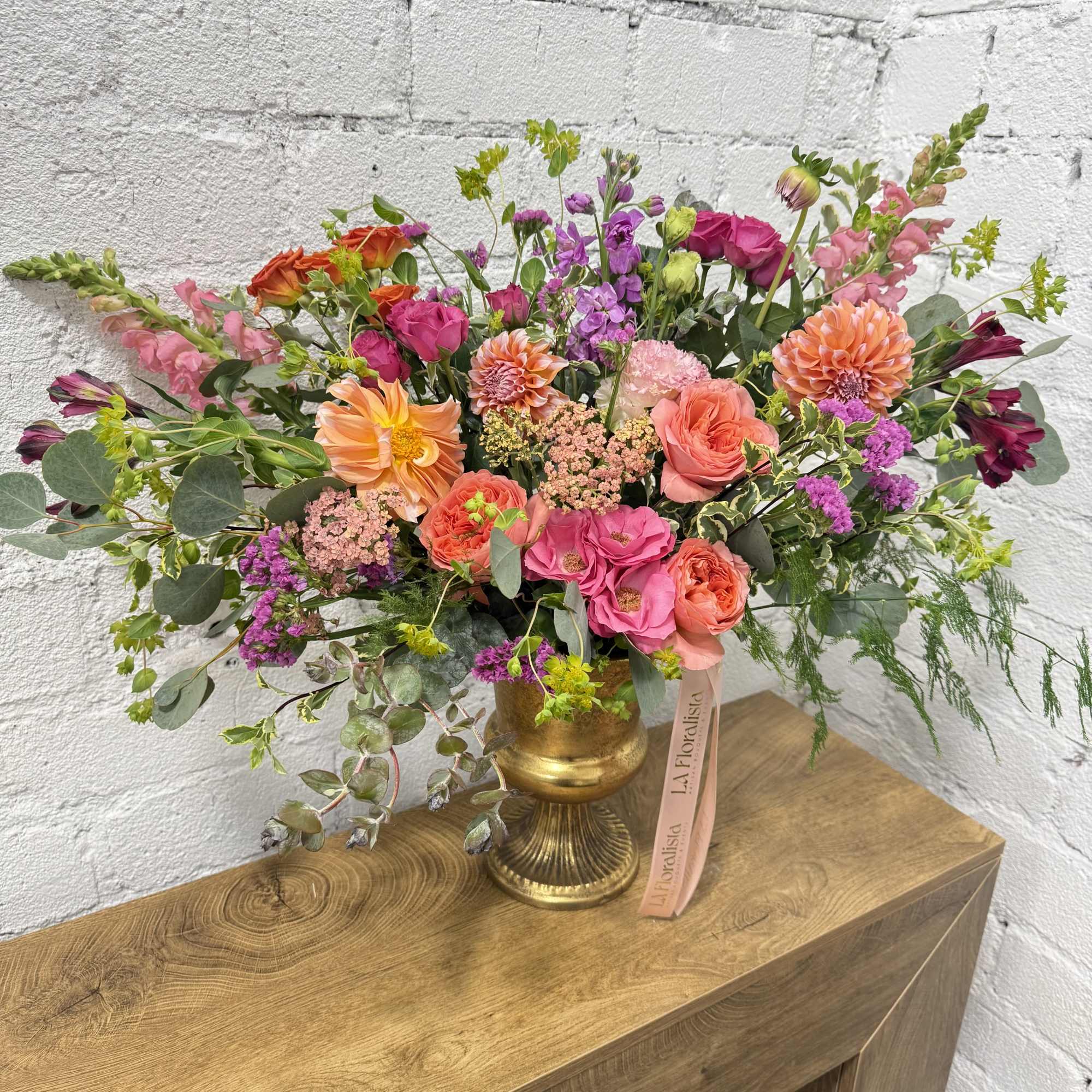 Mixed bouquet of pink, orange, and purple flowers in a gold vase