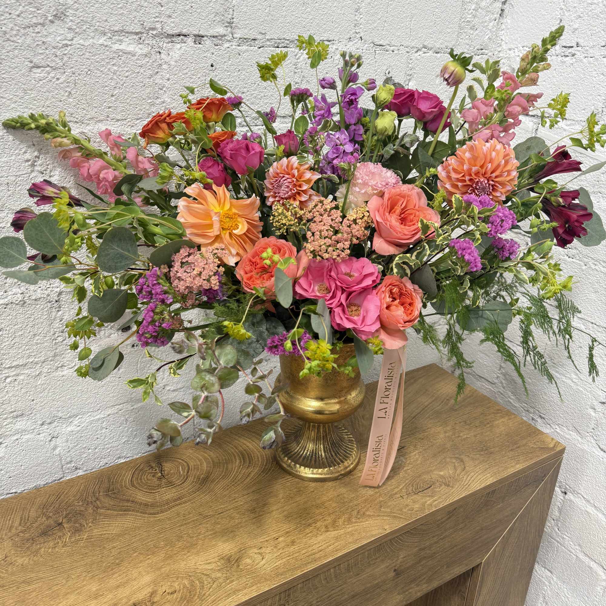 Mixed bouquet of pink, orange, and purple flowers in a gold vase