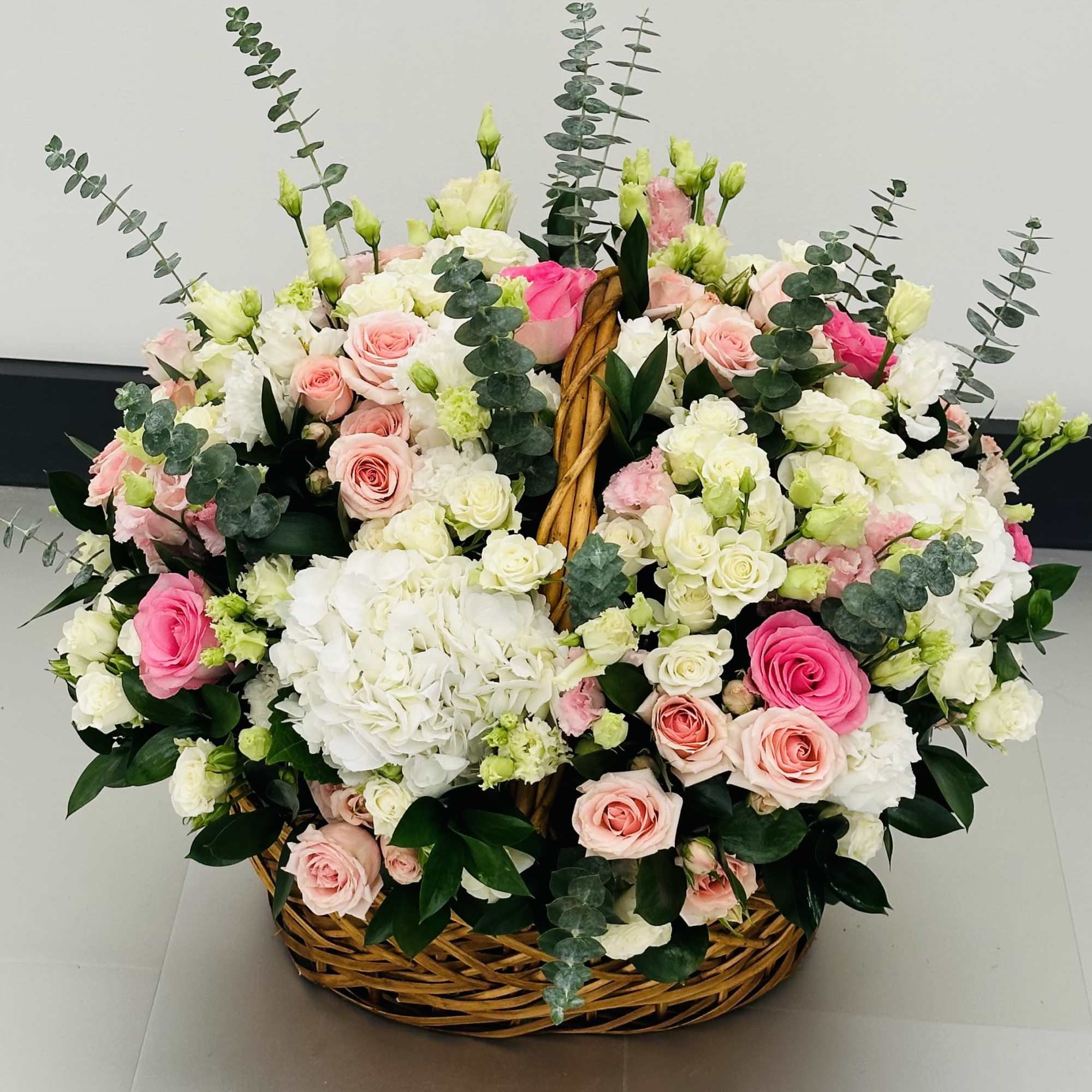 Basket arrangement of pink and white roses with hydrangeas and eucalyptus