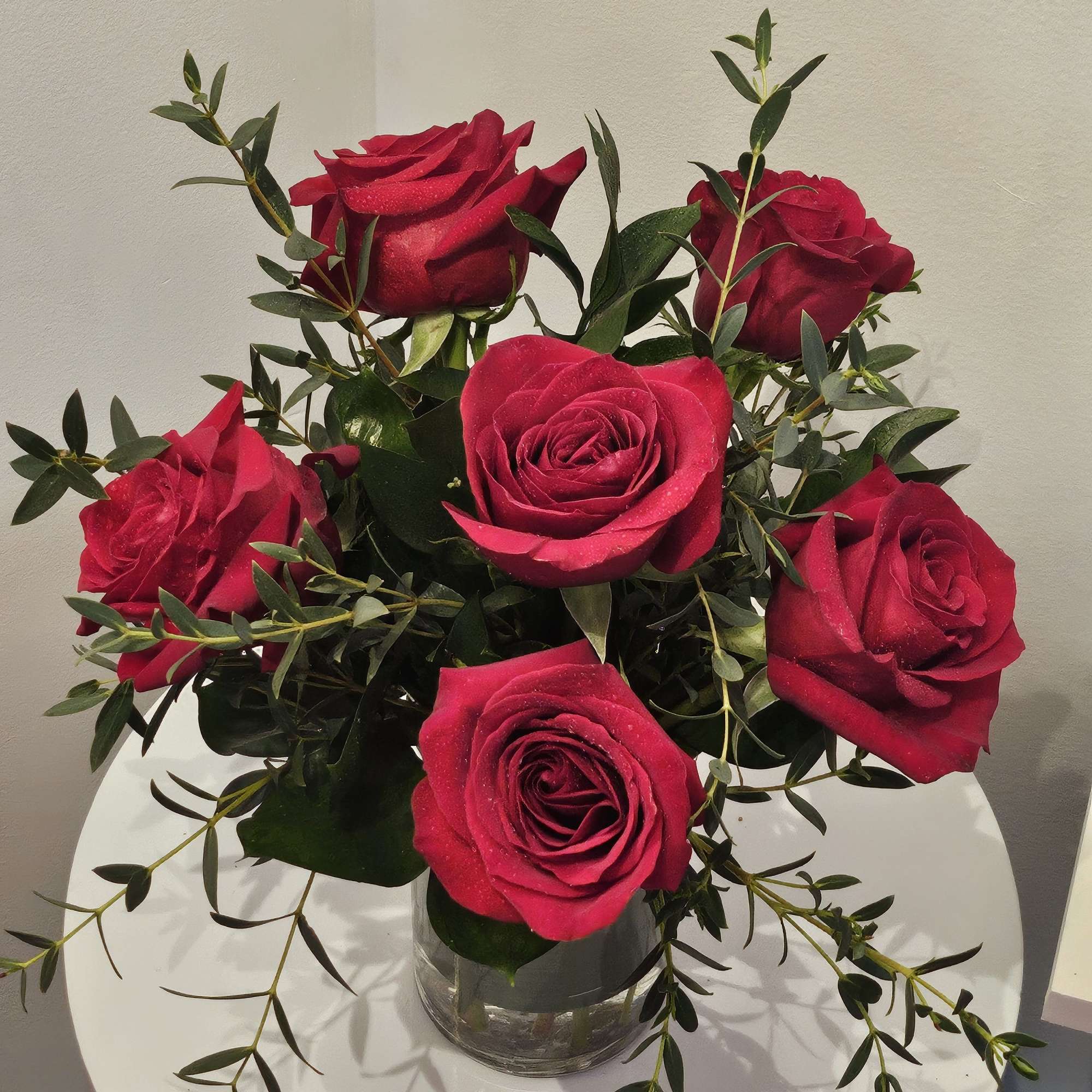 Red roses arranged in a clear glass vase with trailing greenery