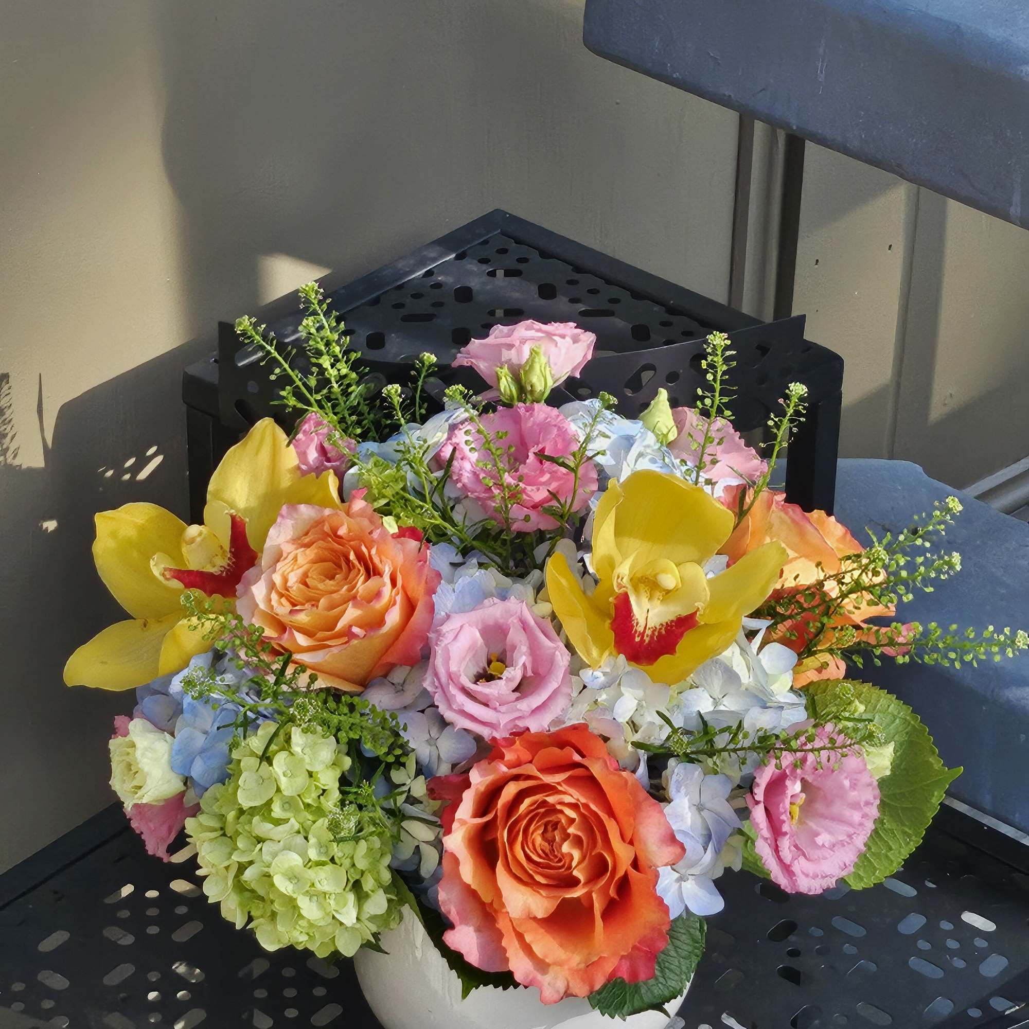Colorful bouquet in a white bowl vase with roses, orchids, and hydrangeas