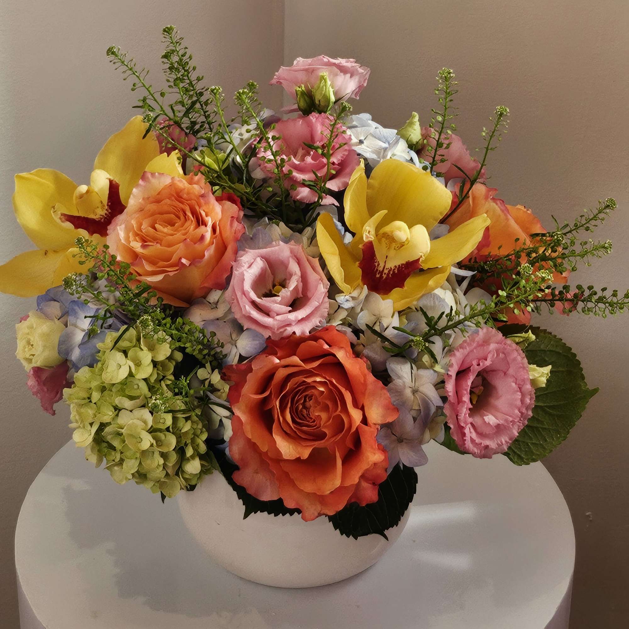Mixed bouquet of roses, orchids, and hydrangeas in a white vase