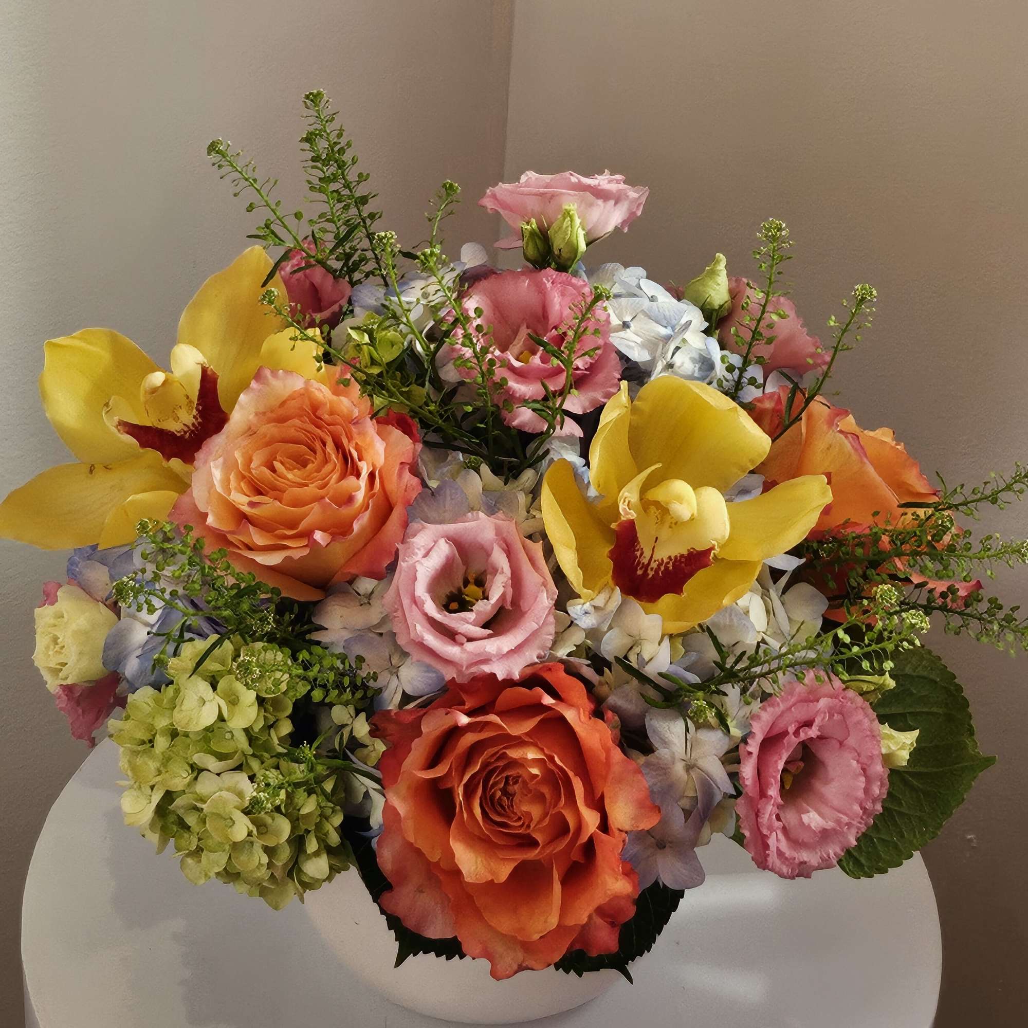 Mixed bouquet in a white vase with roses, orchids, hydrangeas, and yellow blooms