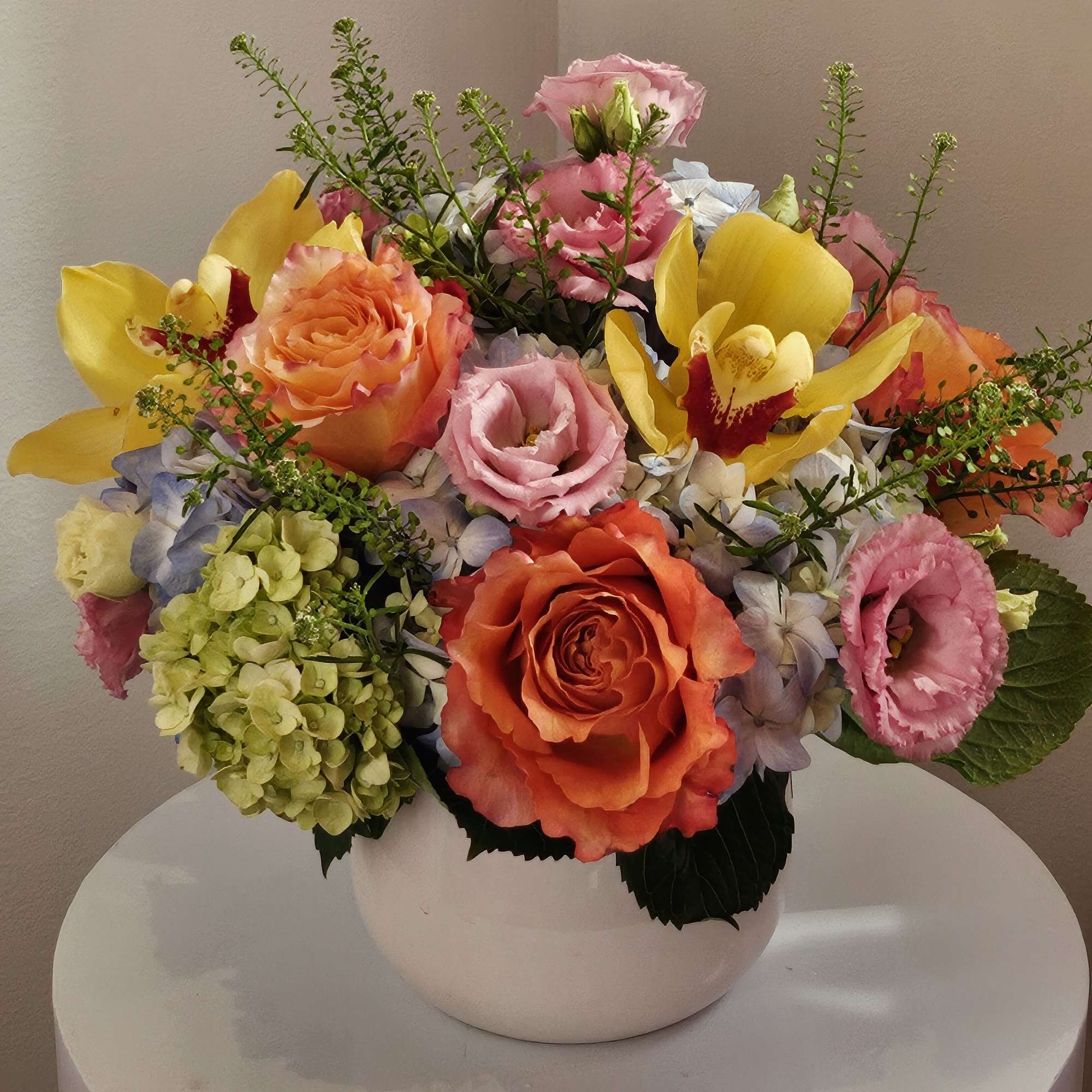 Mixed bouquet of roses, orchids, hydrangea, and calla lilies in a white vase
