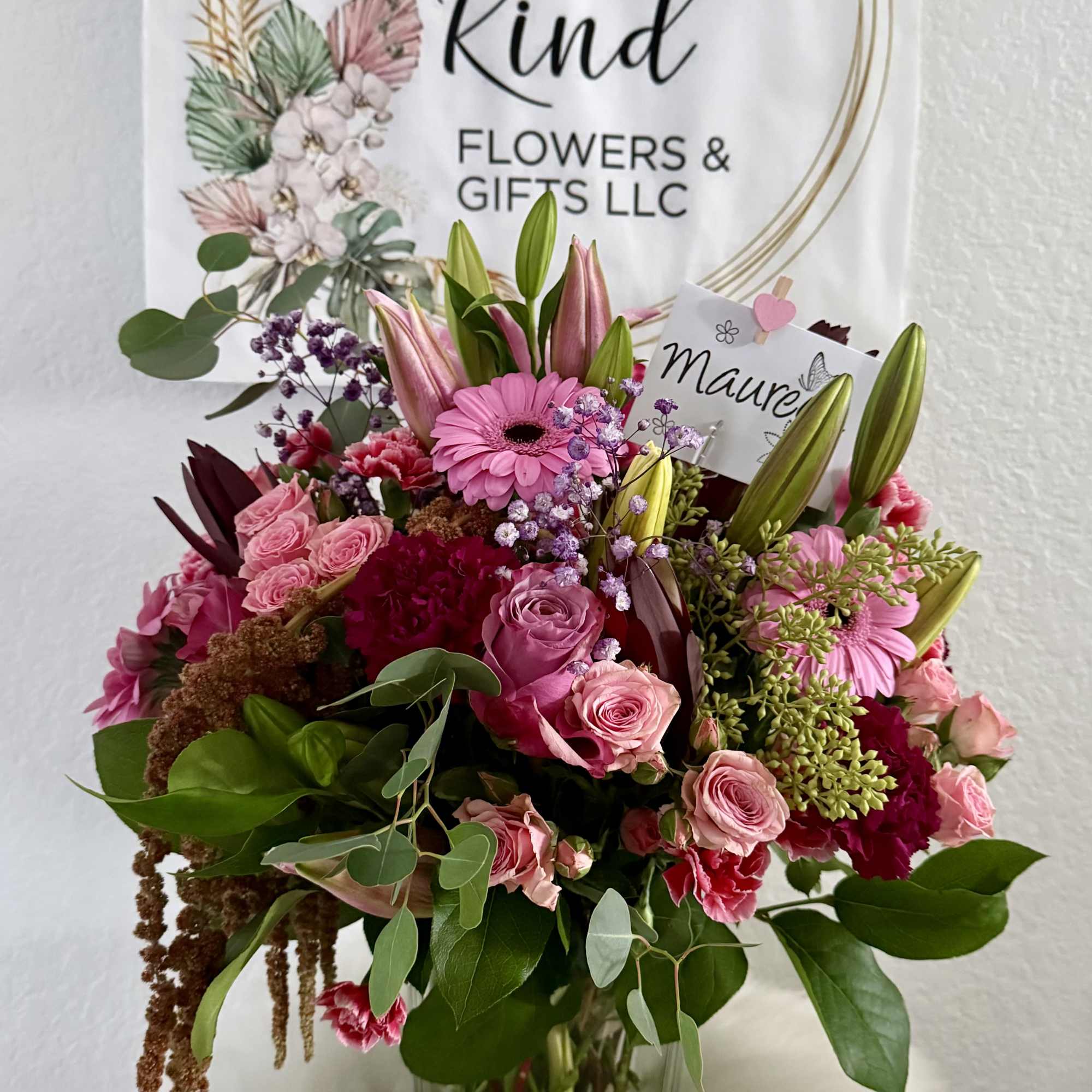 Pink mixed bouquet in a clear glass vase with a sign behind it