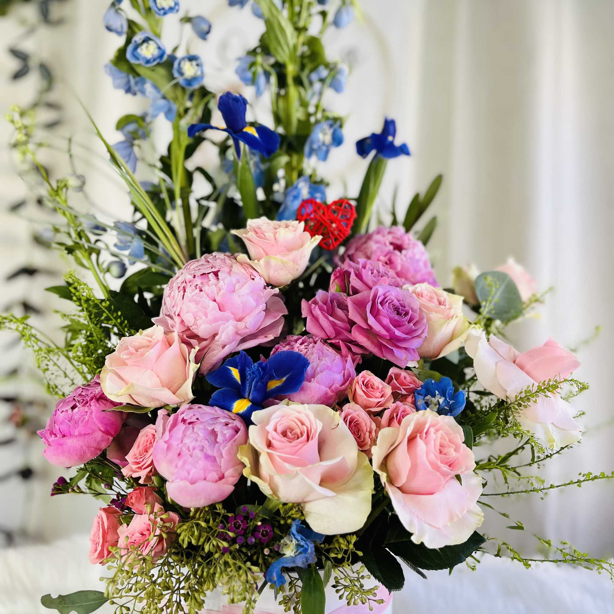 Pink roses and peonies arranged with blue irises in a white hat box