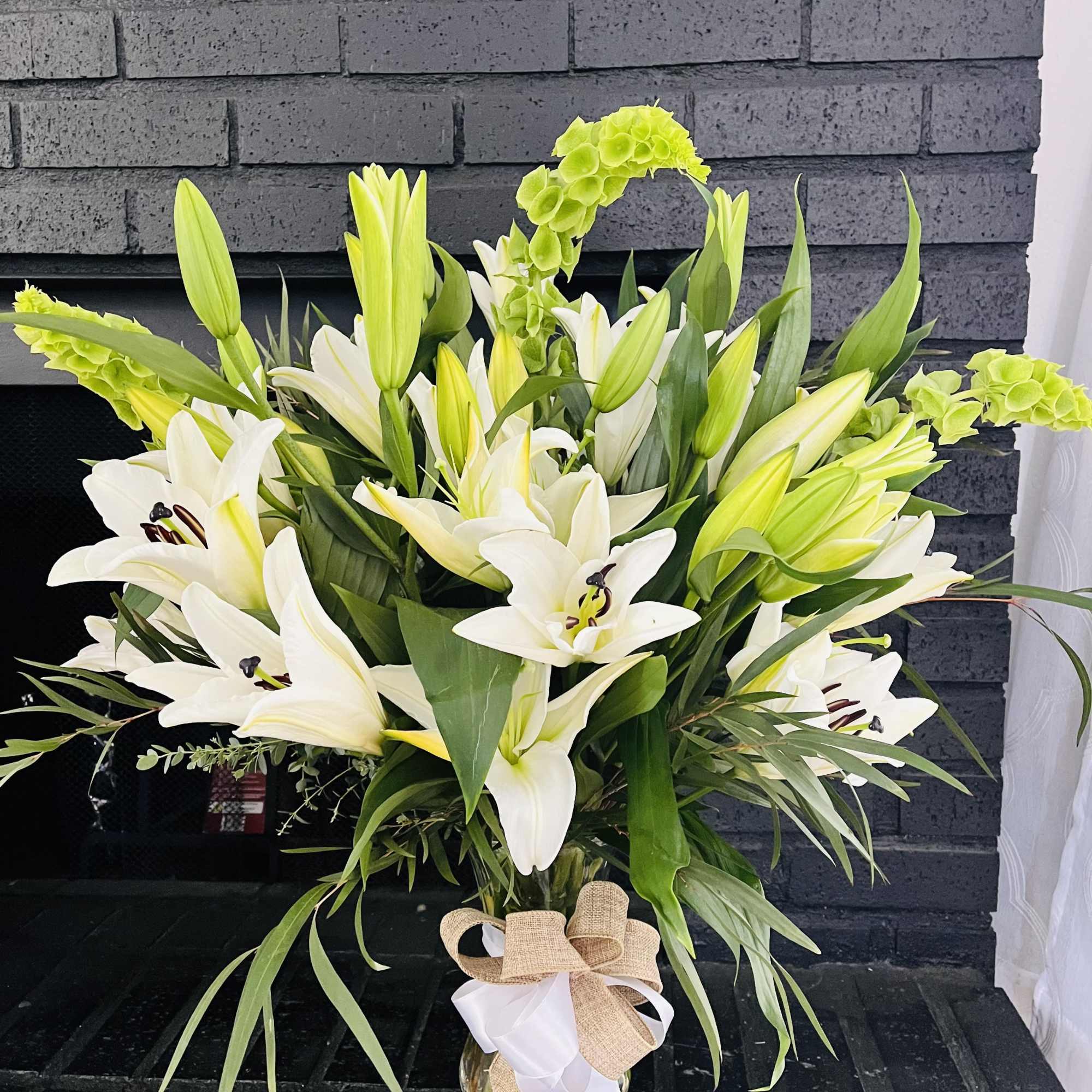 White lilies and green blooms in a glass vase with a burlap bow