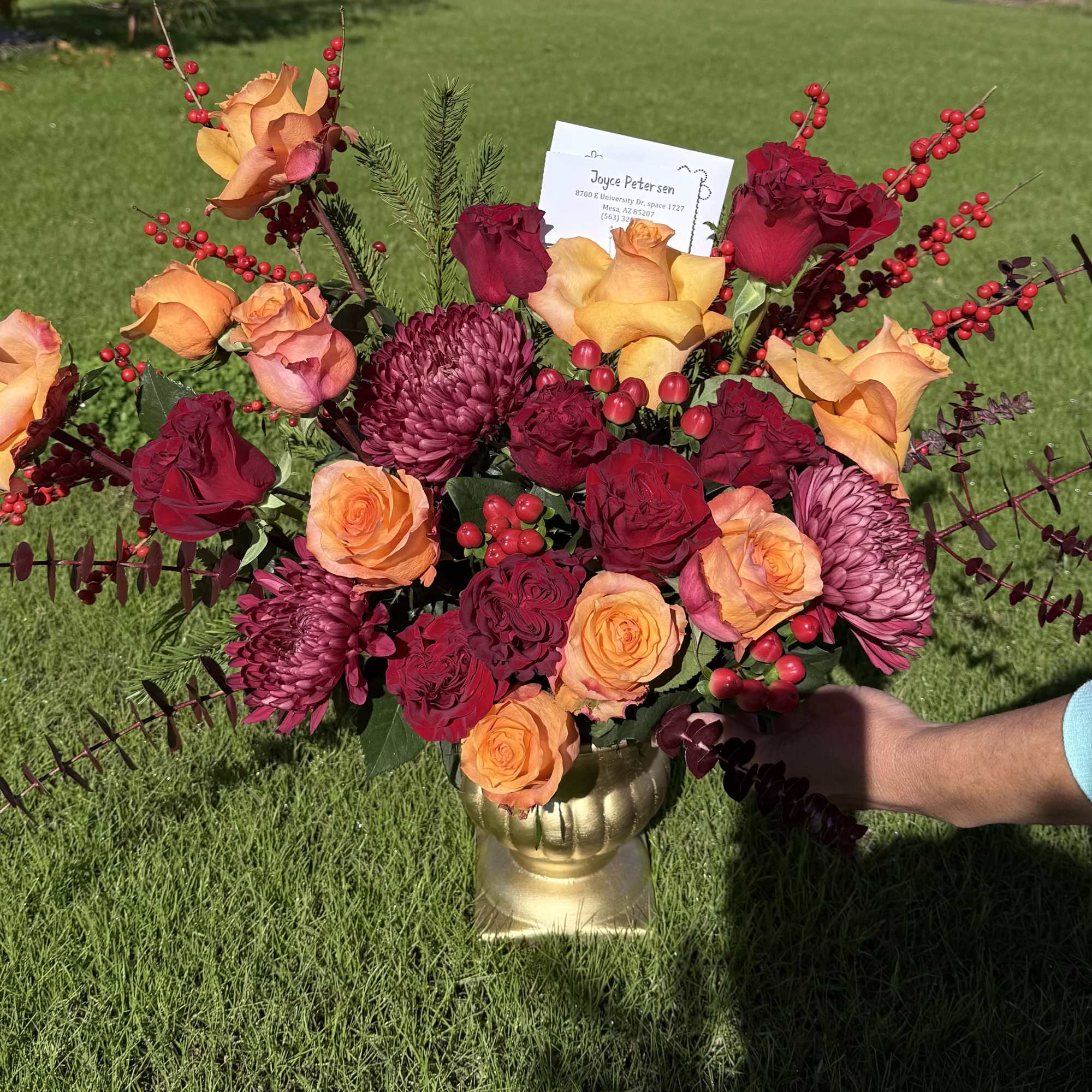 Bouquet of orange and red roses with burgundy mums in a gold vase