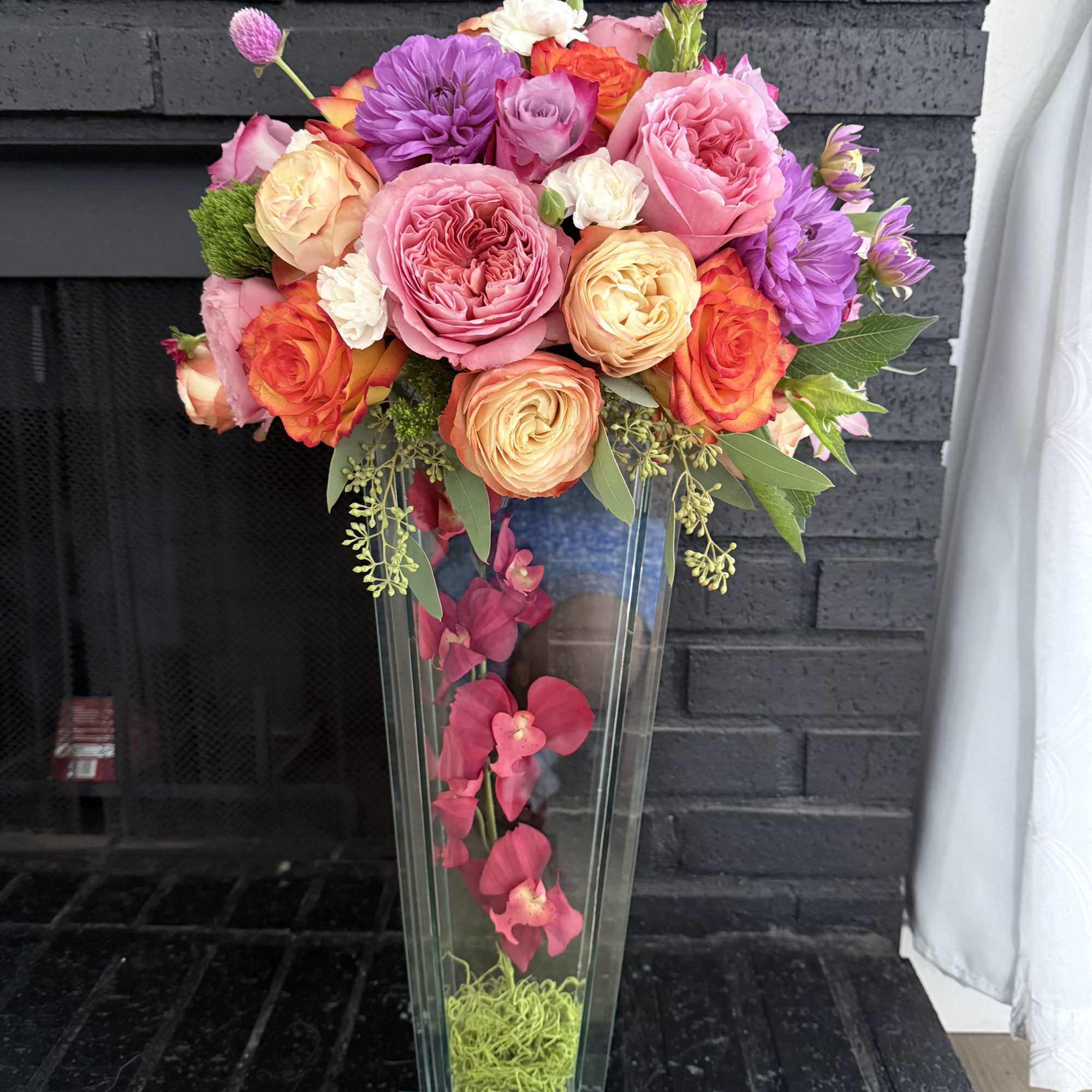 Tall floral arrangement in a clear glass vase with pink, orange, and purple blooms