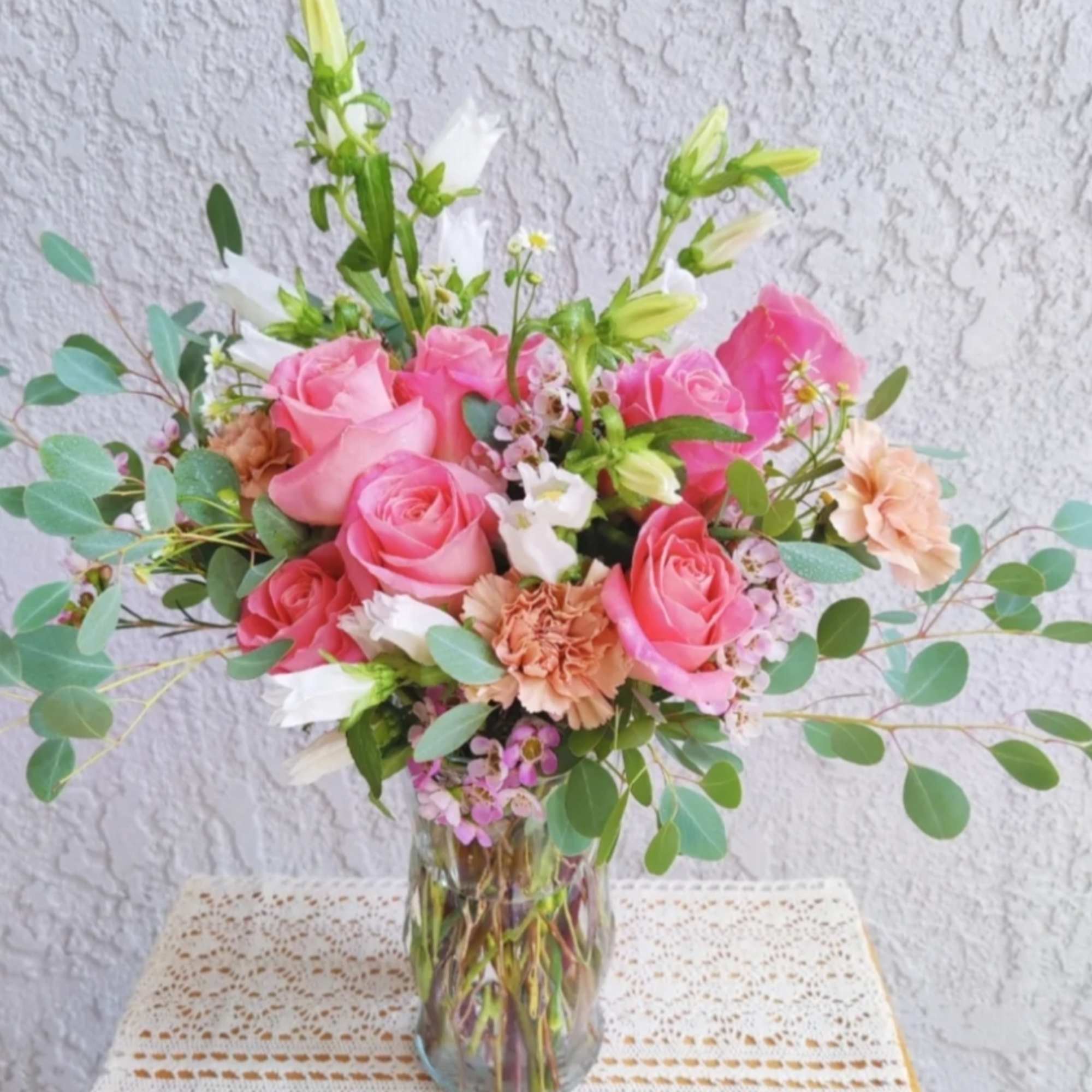 Pink roses and peach carnations in a clear glass vase with airy greenery