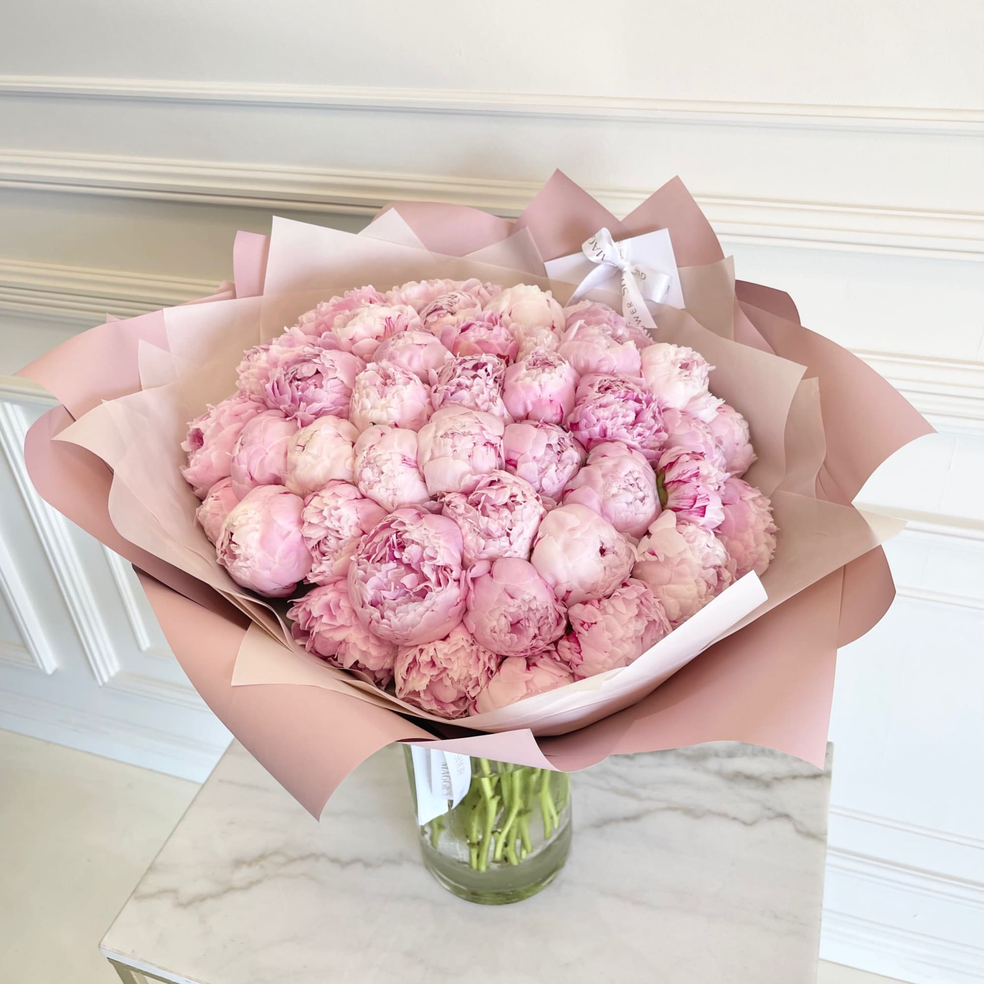Bouquet of pale pink peonies wrapped in blush paper in a glass vase