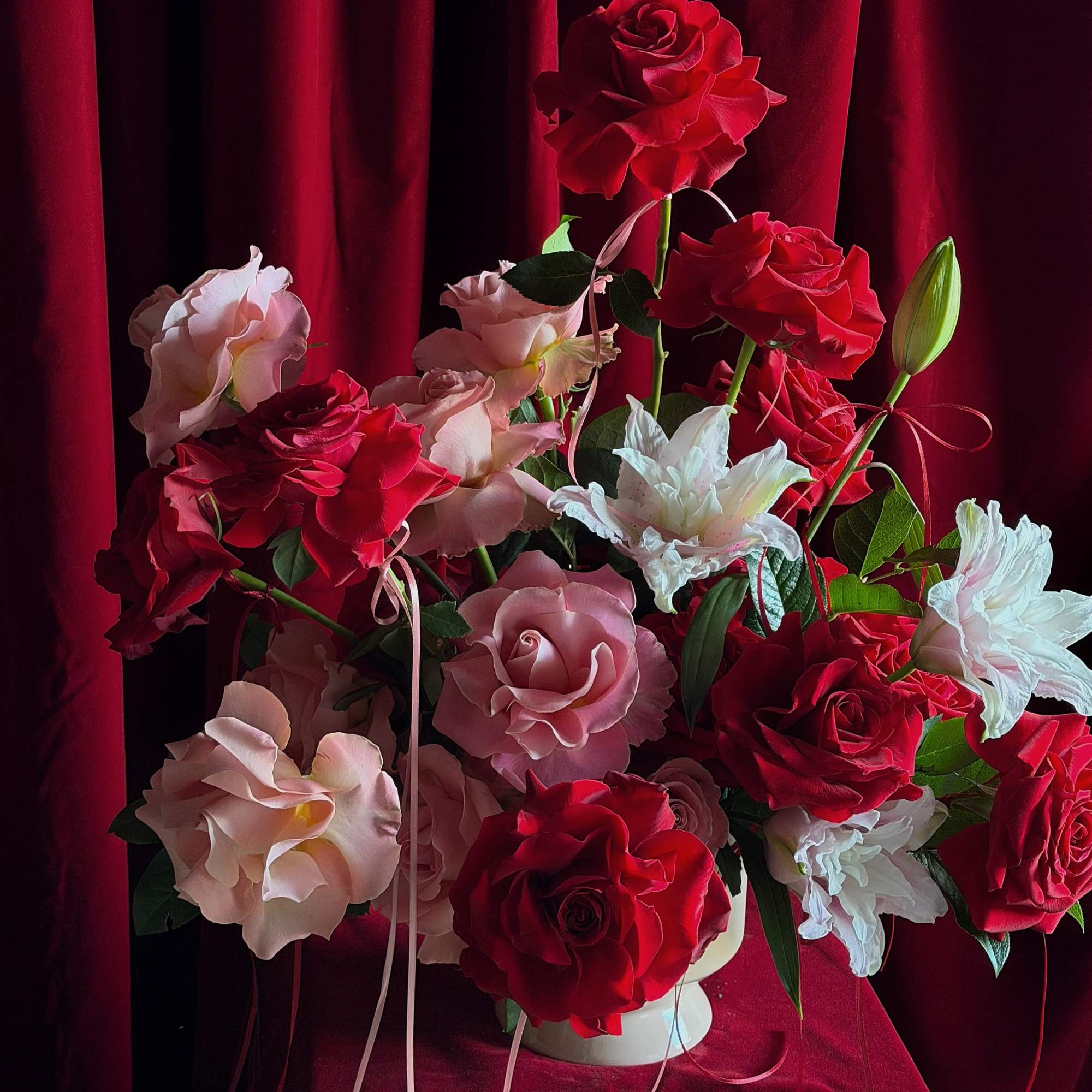 Red and blush roses arranged in a white vase against a red velvet backdrop