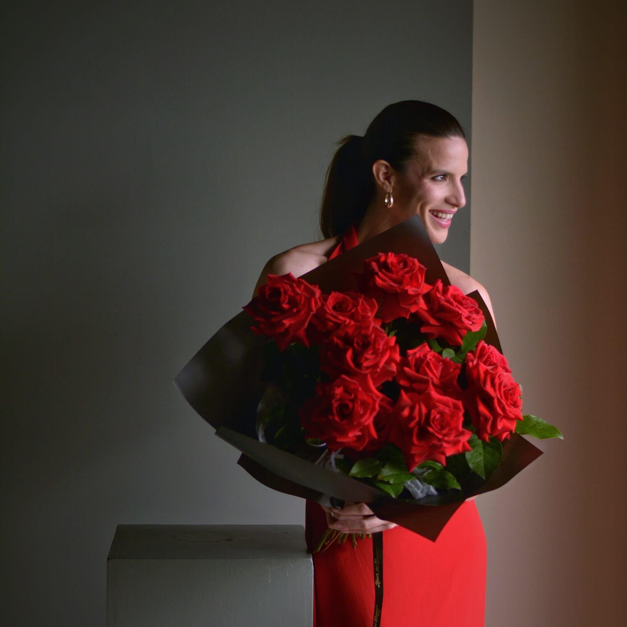 Woman holding a large bouquet of red roses wrapped in dark paper