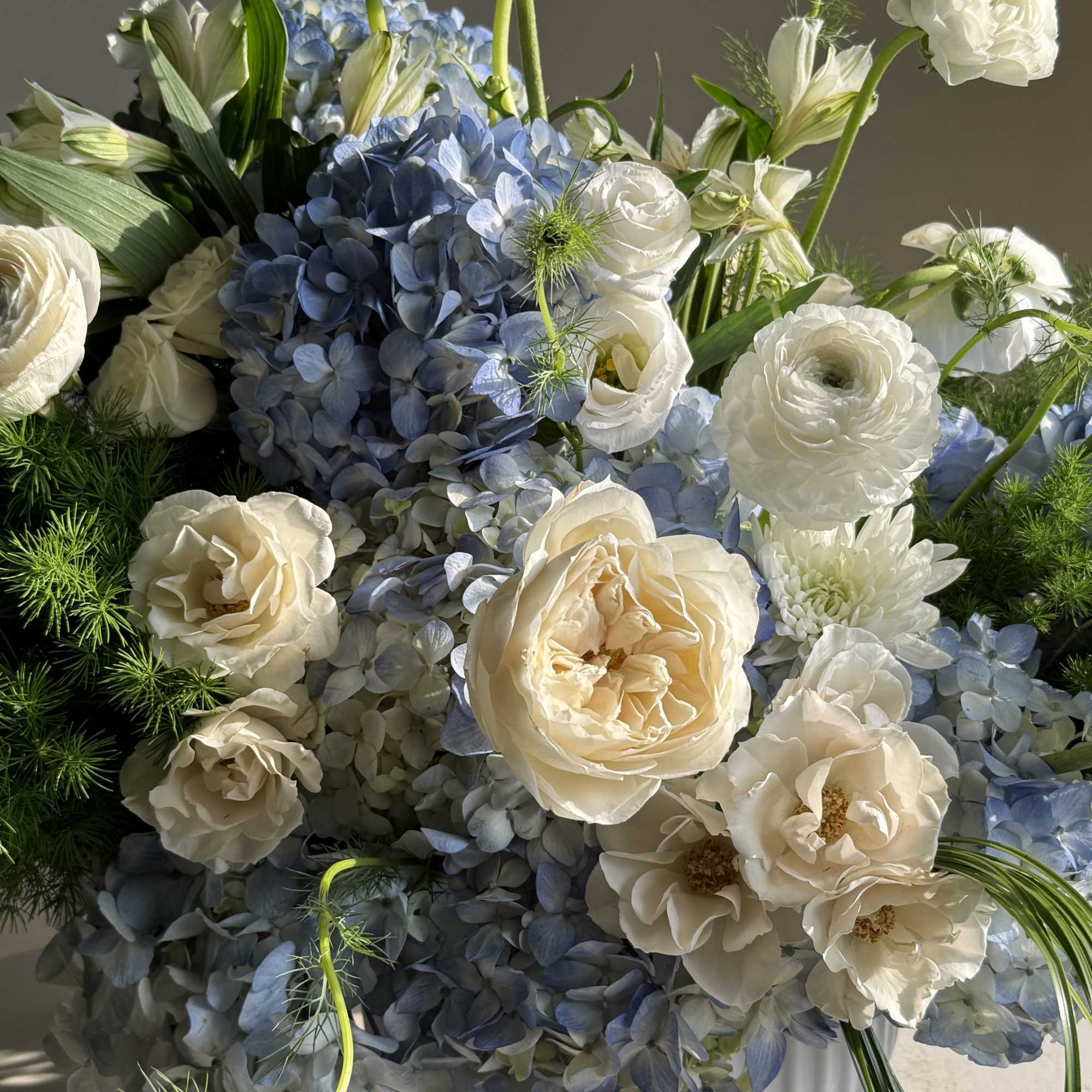 Blue hydrangeas and white roses arranged in a white vase