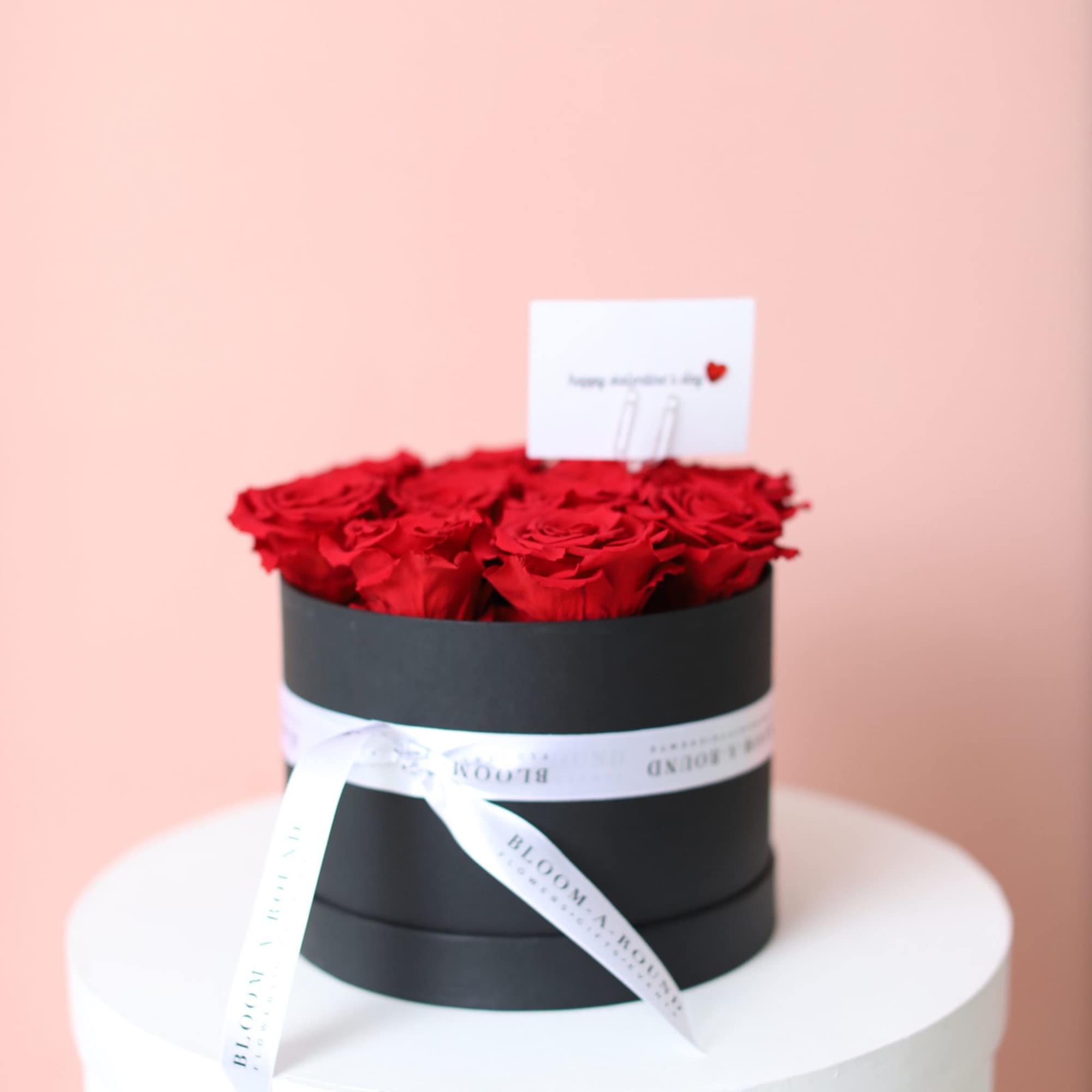 Red roses arranged in a black round box with a white ribbon