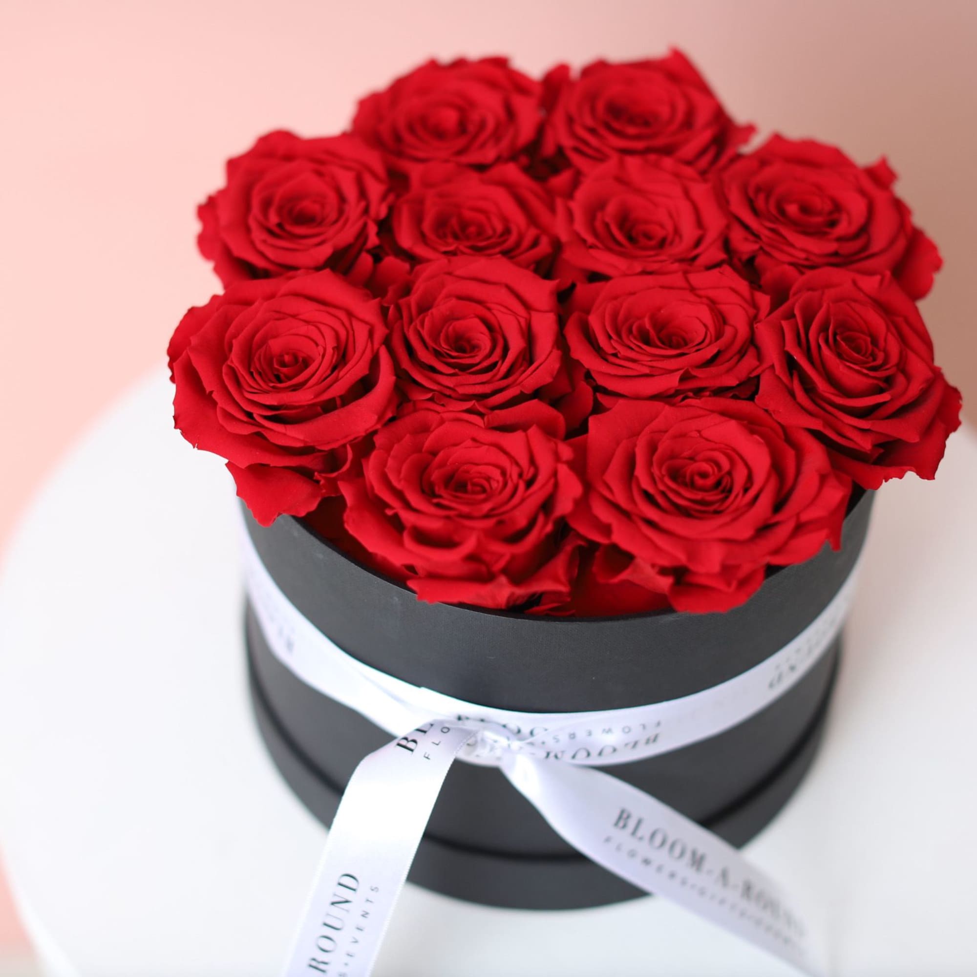 Red roses arranged in a black round box with a white ribbon