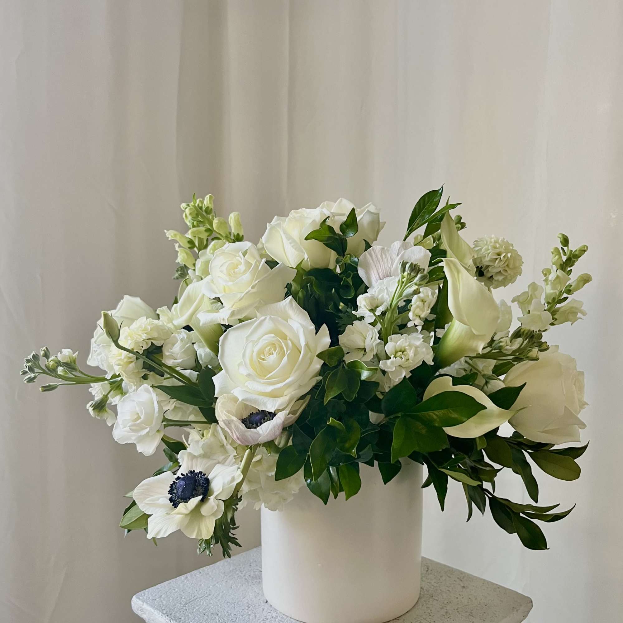 White floral arrangement in a white vase with roses and calla lilies