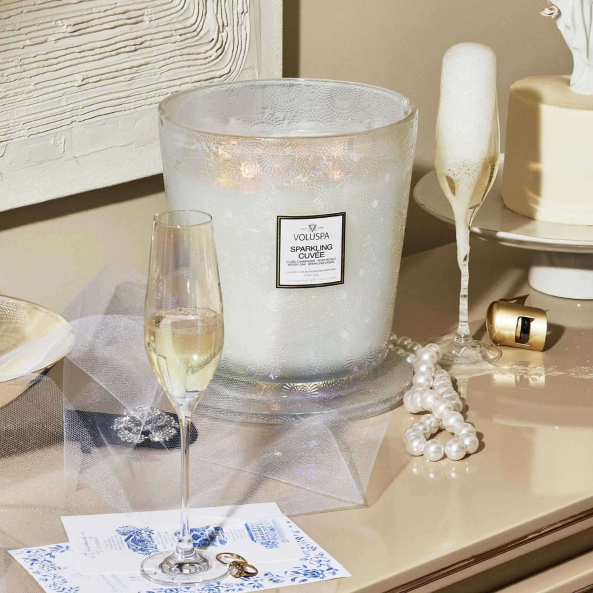 Champagne candle in a frosted glass jar with a flute of sparkling drink and pearl beads