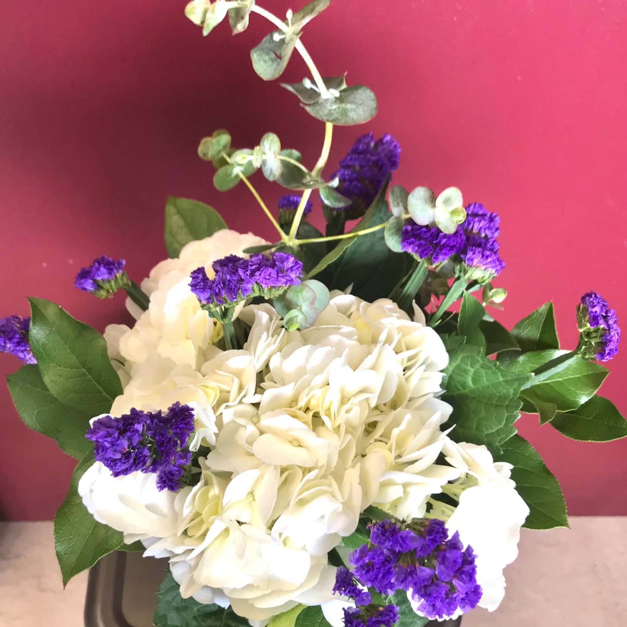 White hydrangea bouquet with purple filler flowers in a container