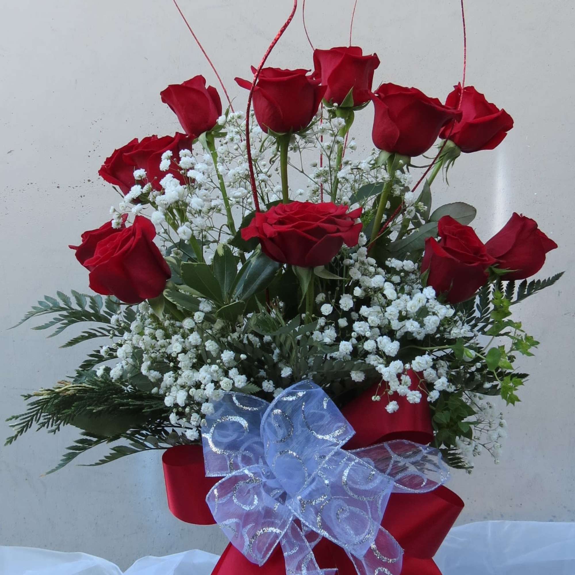Red roses arranged in a glass vase with white baby's breath and a red ribbon bow.