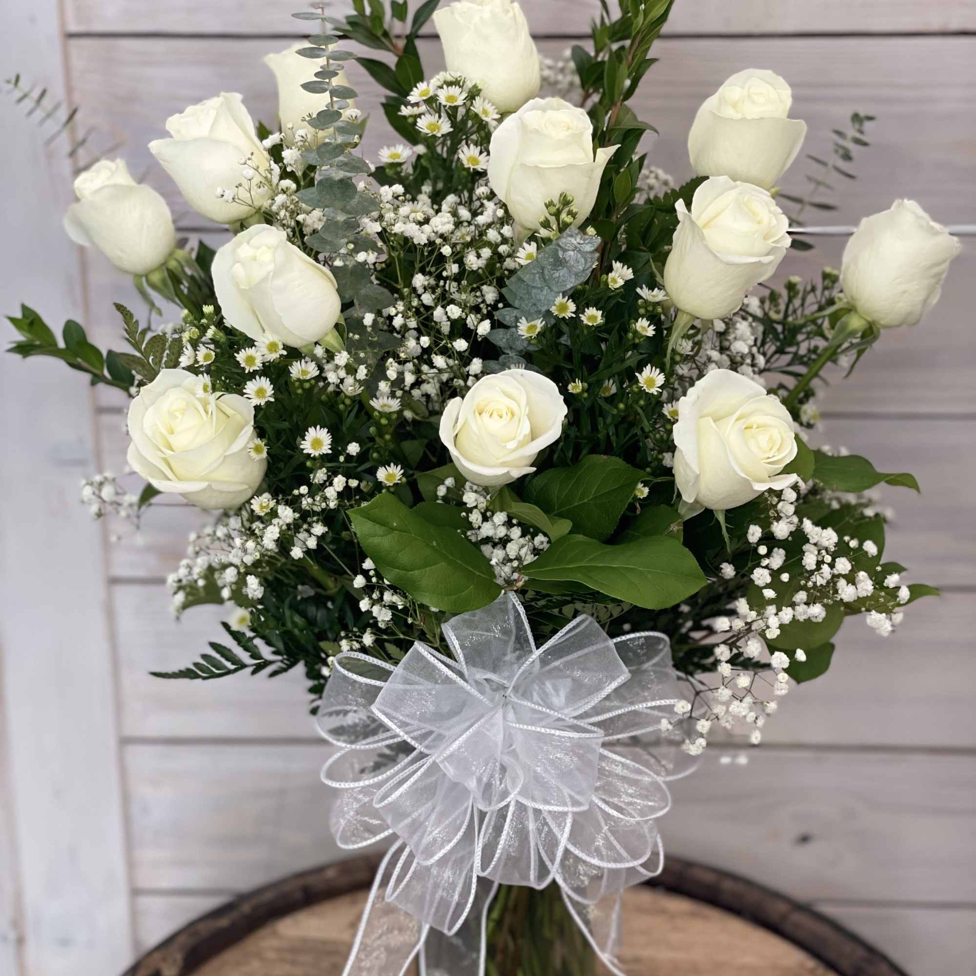 White roses in a glass vase with baby's breath and a white ribbon bow