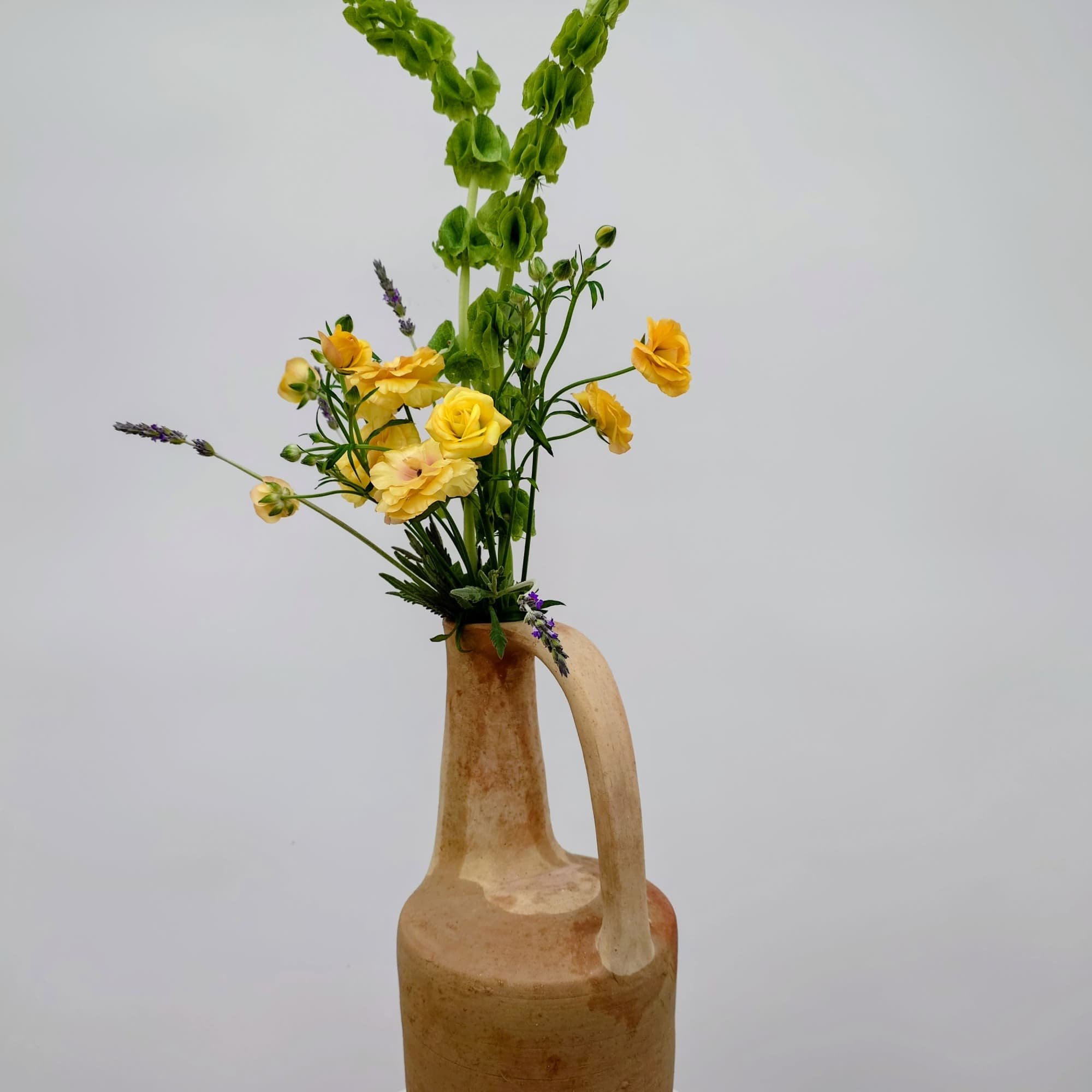 A sculptural floral arrangement designed in a tall, long-necked clay pitcher, Juno