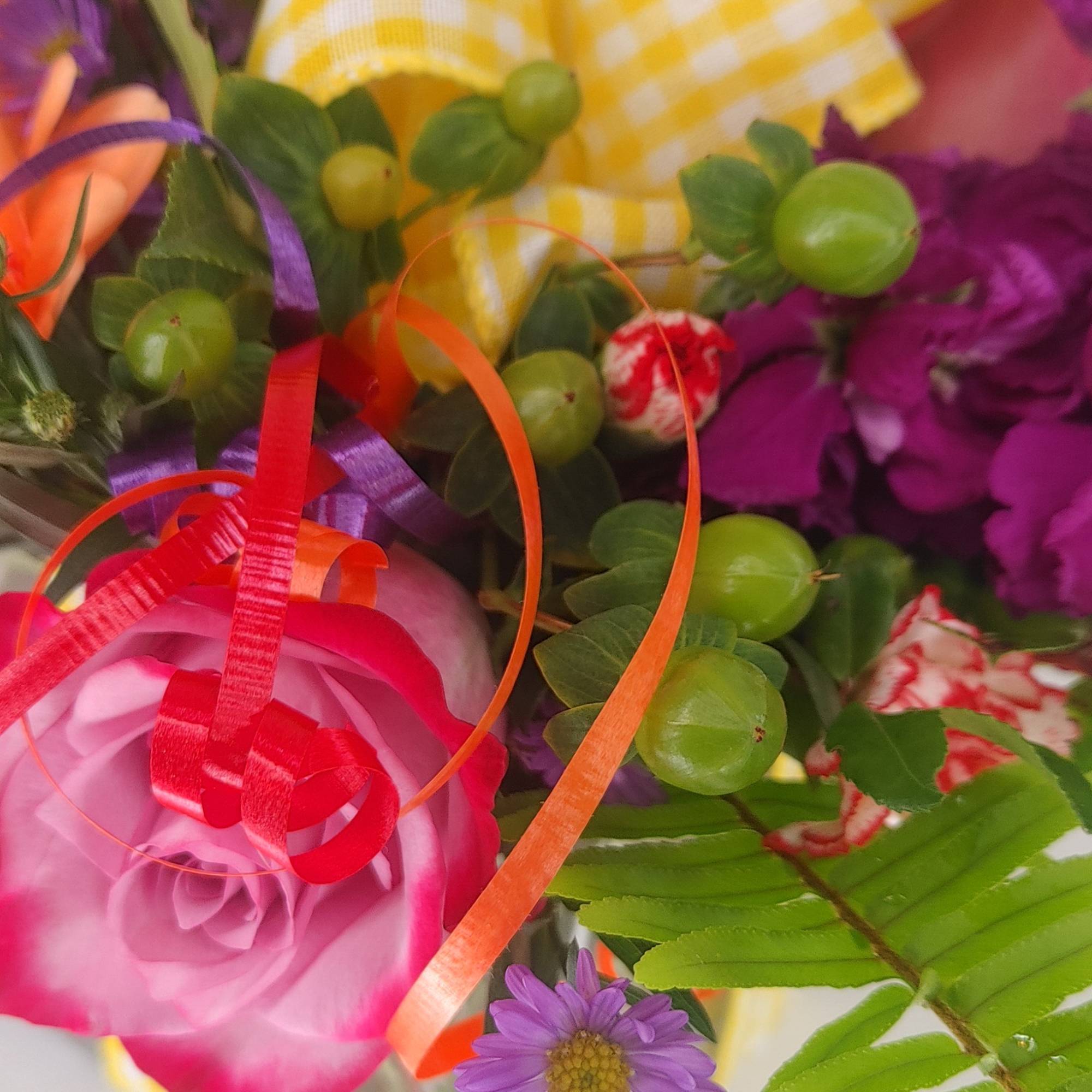 Close-up bouquet with a pink rose, purple daisy, and ribbon accents