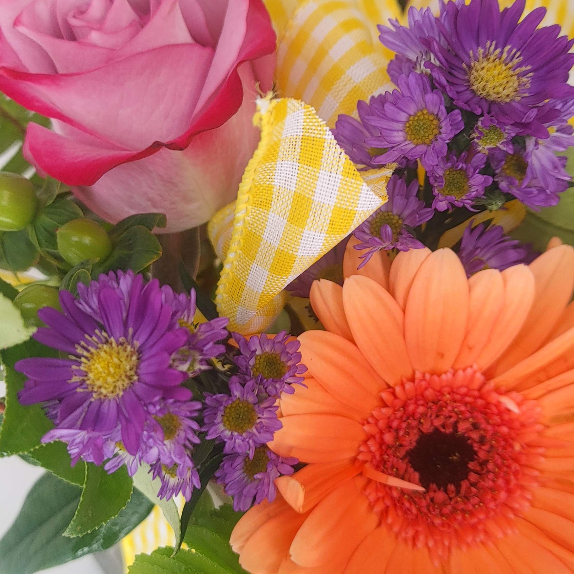 Close-up bouquet with a pink rose, purple daisies, and an orange gerbera daisy