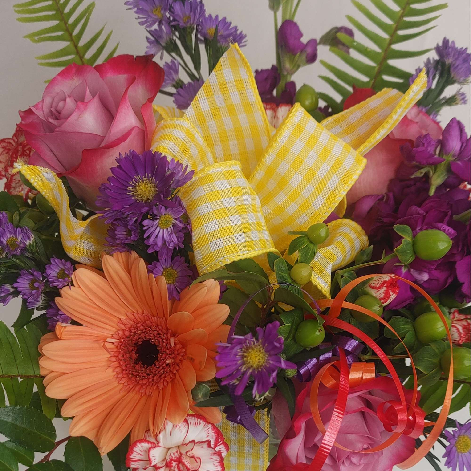 Mixed bouquet with pink roses, orange gerbera daisies, and purple daisies in a glass vase