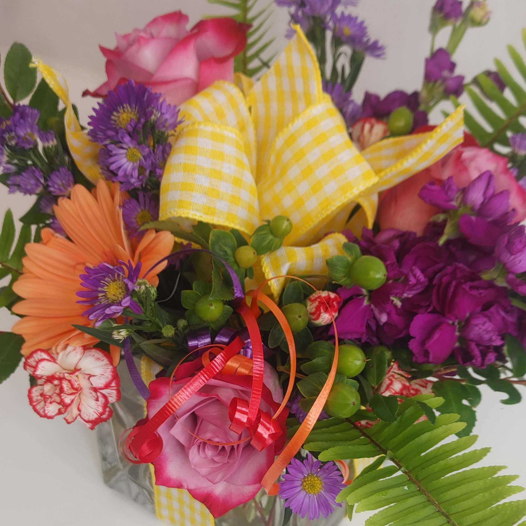 Mixed bouquet of pink roses, purple daisies, and orange gerbera daisies in a glass vase