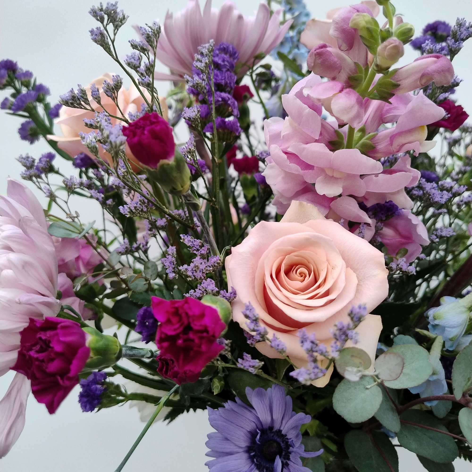 Mixed bouquet with pink roses, purple blooms, and a glass vase
