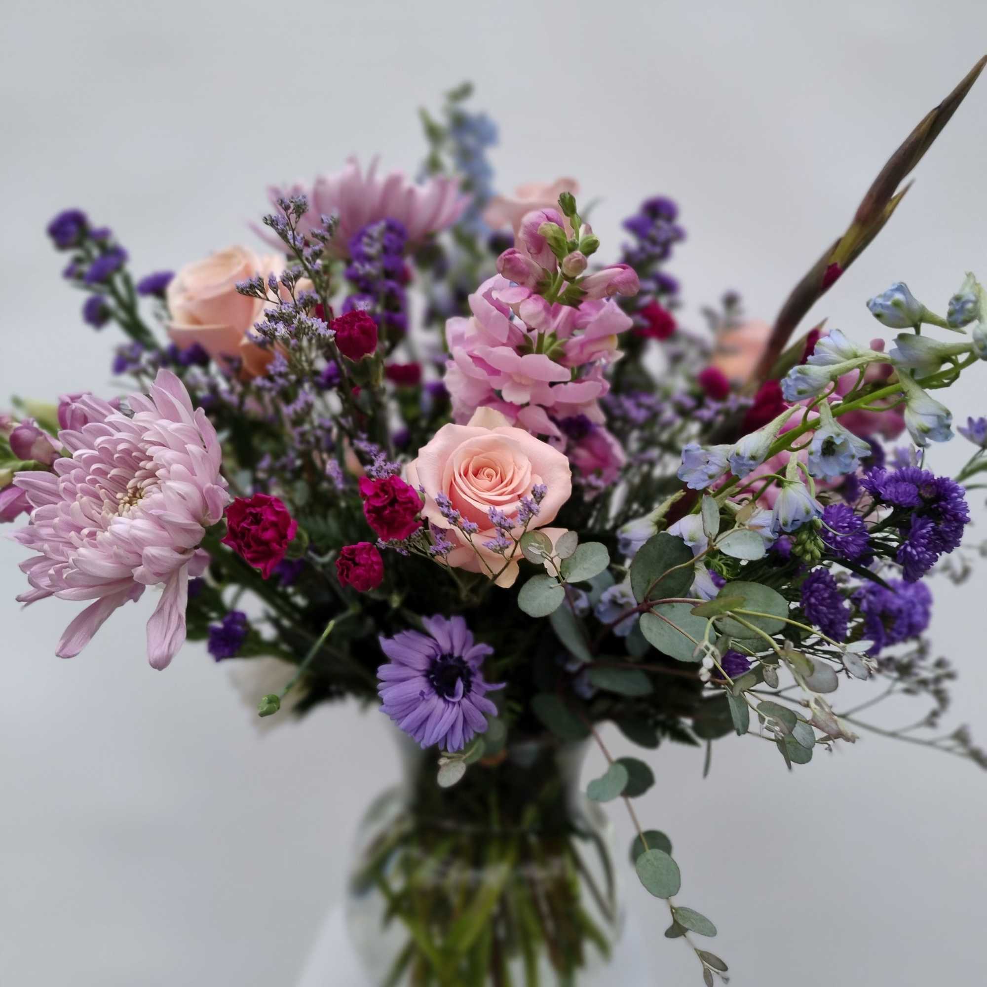 Mixed bouquet of pink, purple, and peach flowers in a glass vase