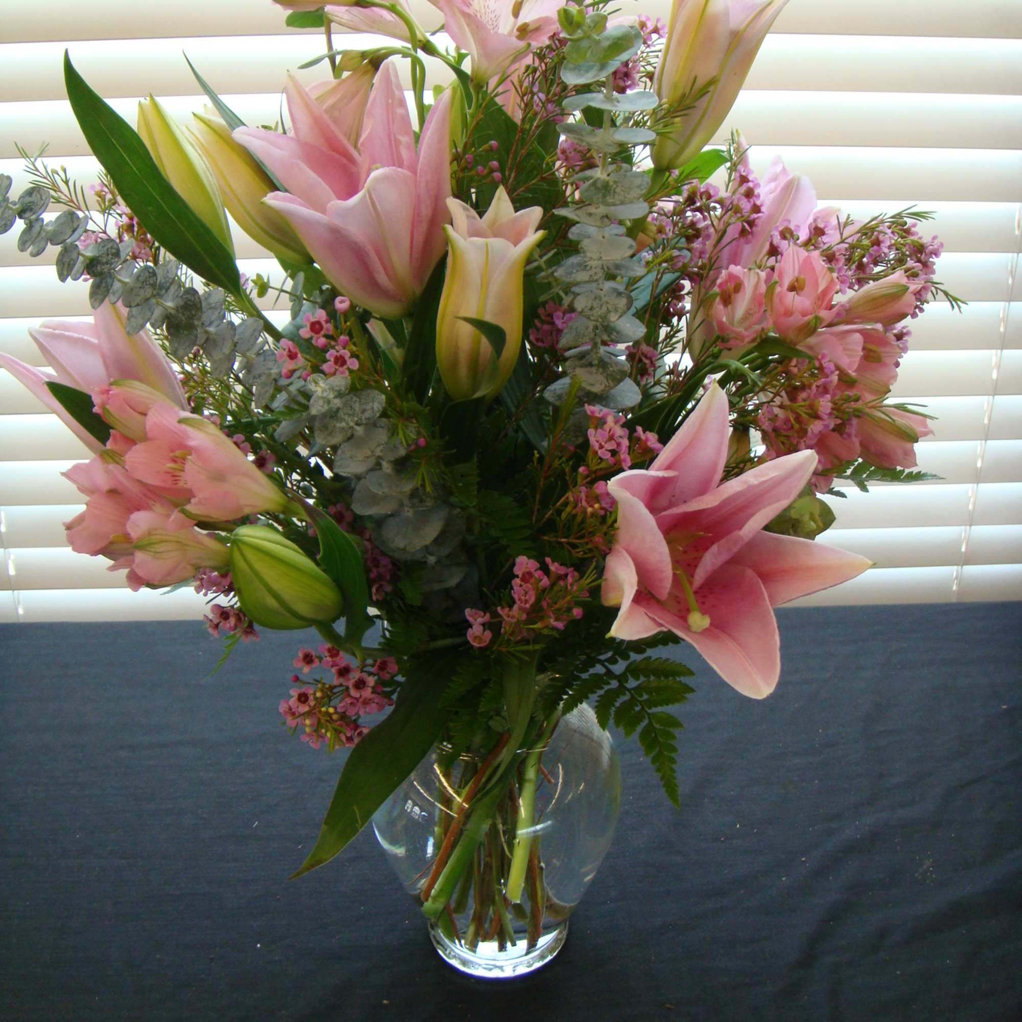 Pink lilies and small pink filler flowers in a clear glass vase
