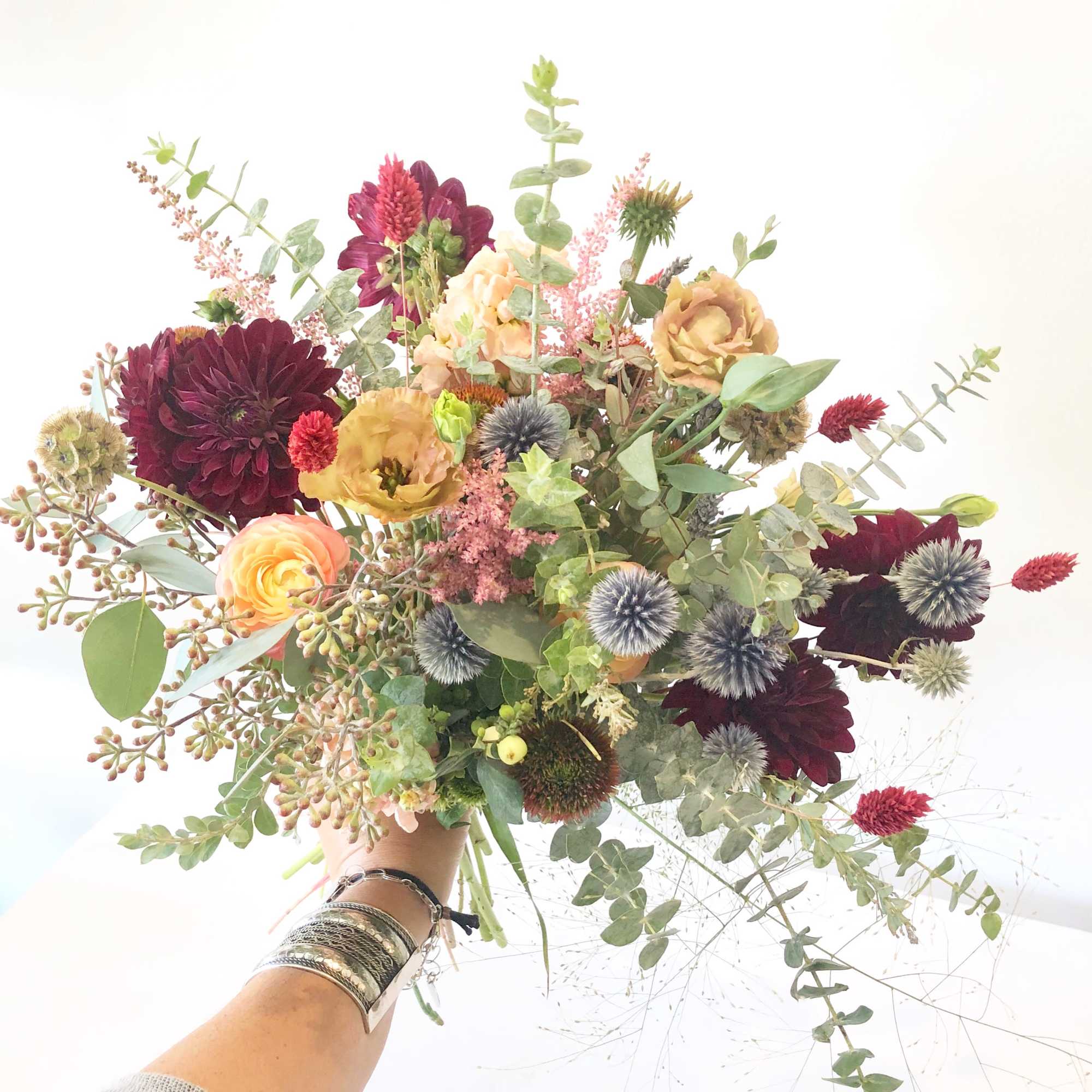Handheld bouquet of burgundy, peach, and green flowers with airy foliage