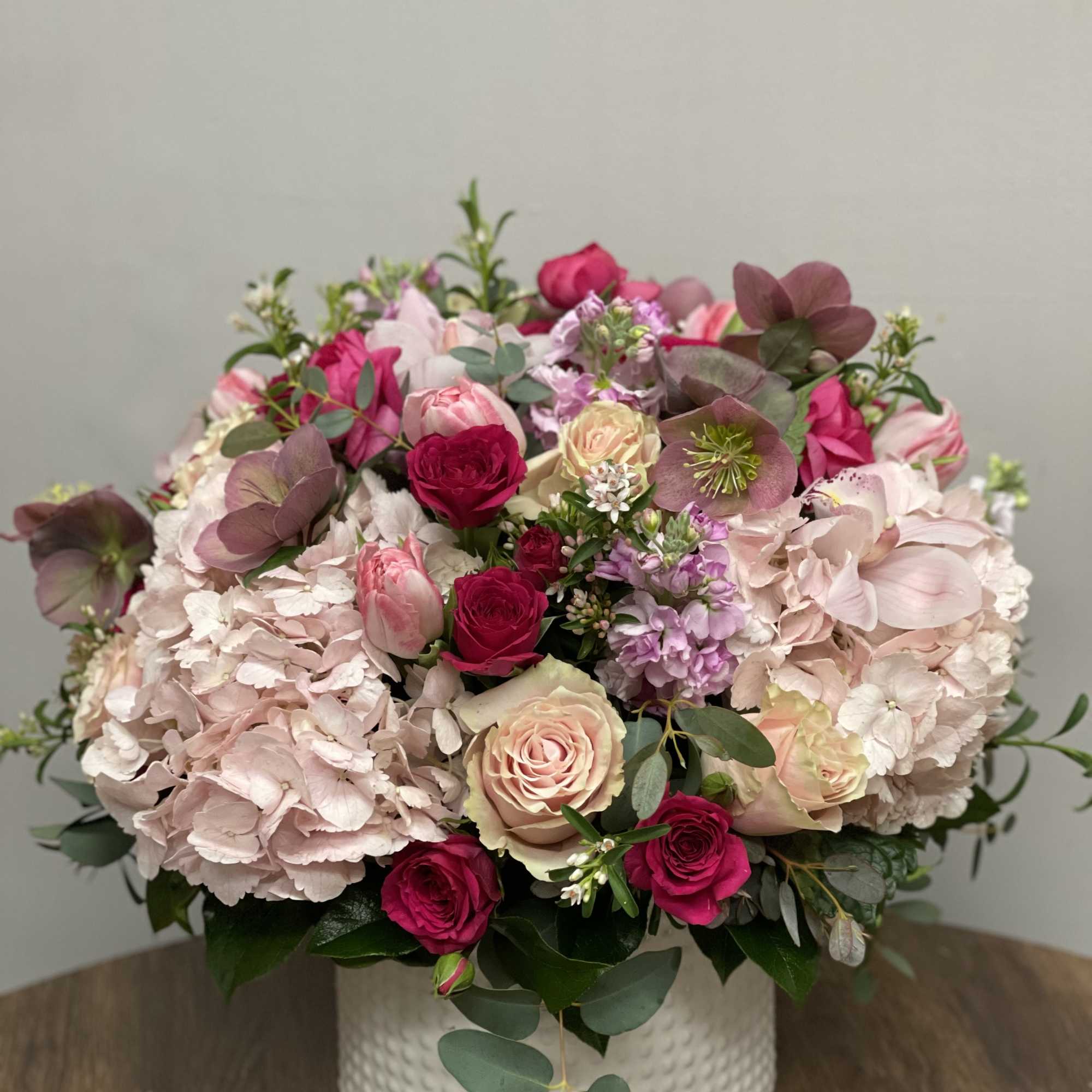 Round arrangement of pink hydrangeas and roses in a white ceramic vase
