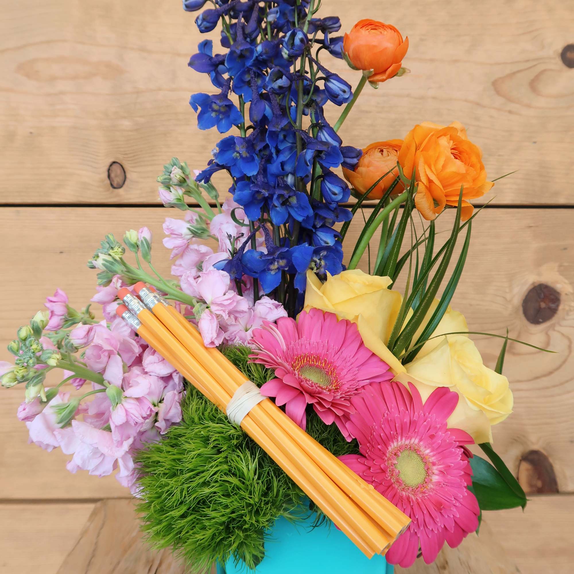 Colorful bouquet in a turquoise vase with blue, pink, yellow, and orange flowers