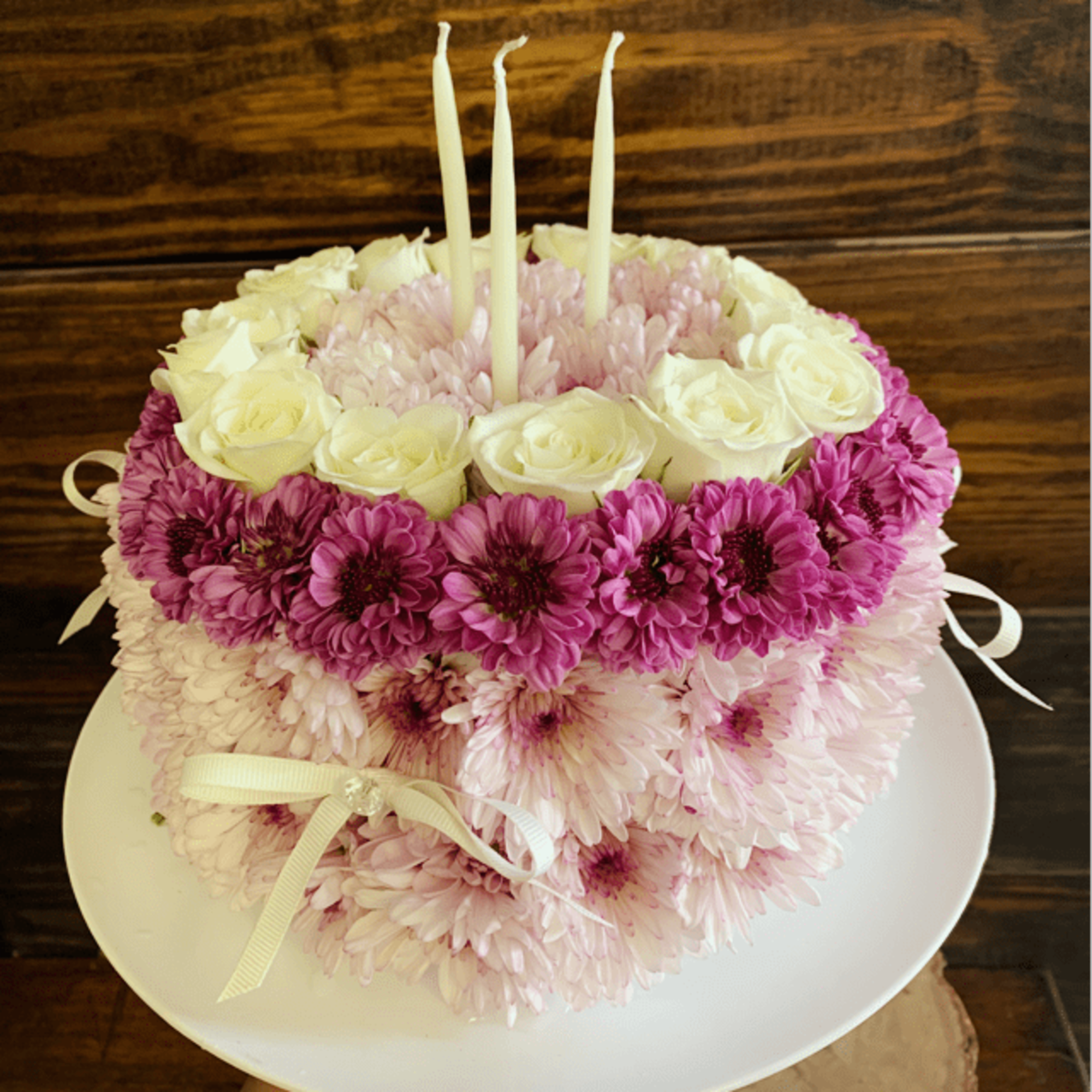 Round floral cake with pink and white flowers and three candles