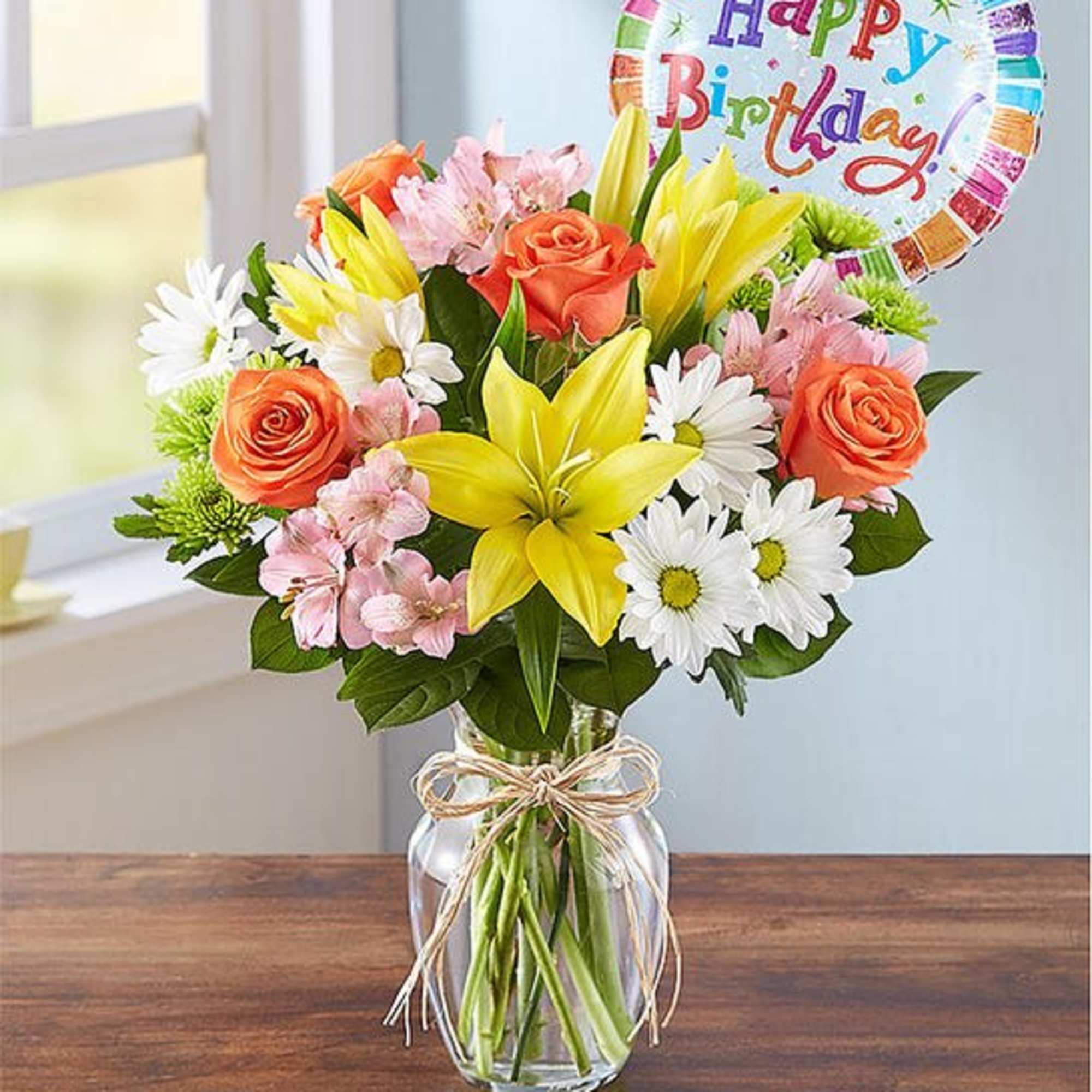Birthday bouquet of roses, lilies, and daisies in a glass vase with a balloon