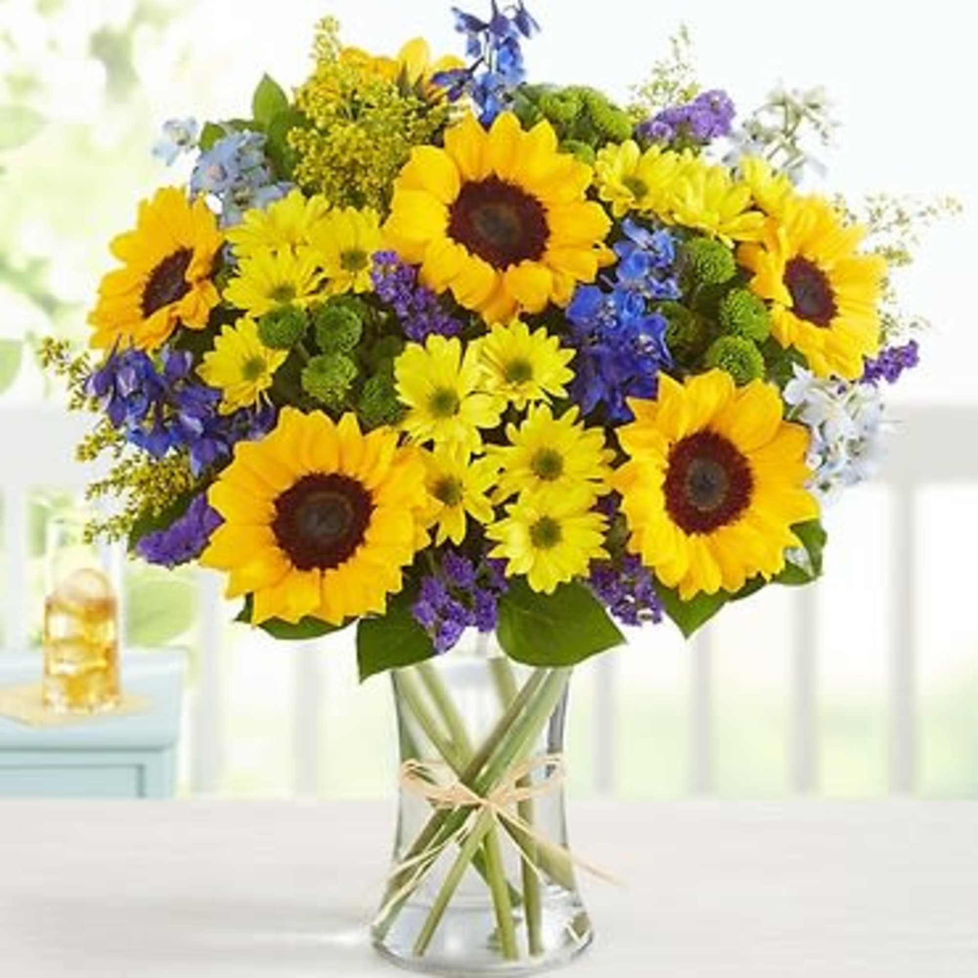 Bouquet of sunflowers, yellow daisies, and purple flowers in a glass vase